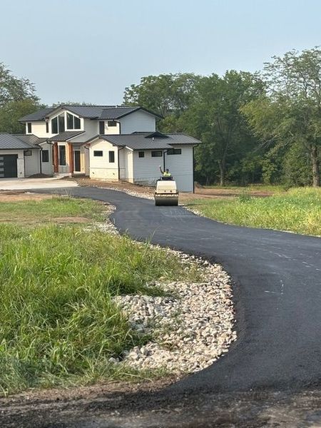Asphalt driveway leading to a modern house with a rolling machine compacting the surface.