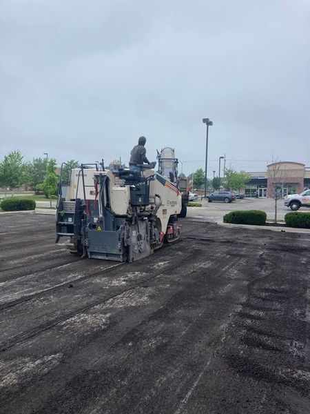 Asphalt milling machine removing old pavement in a parking lot; a person operates the machinery.