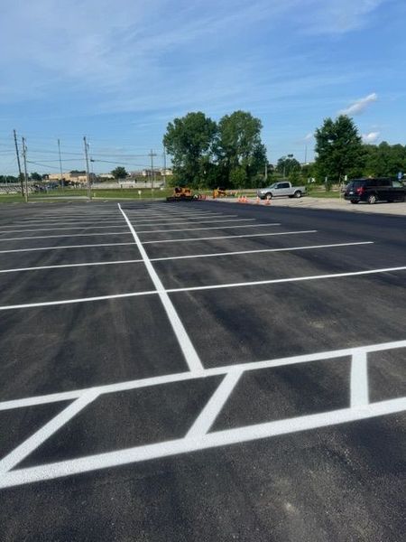Newly painted parking lot with white lines, under a blue sky with trees in the background.