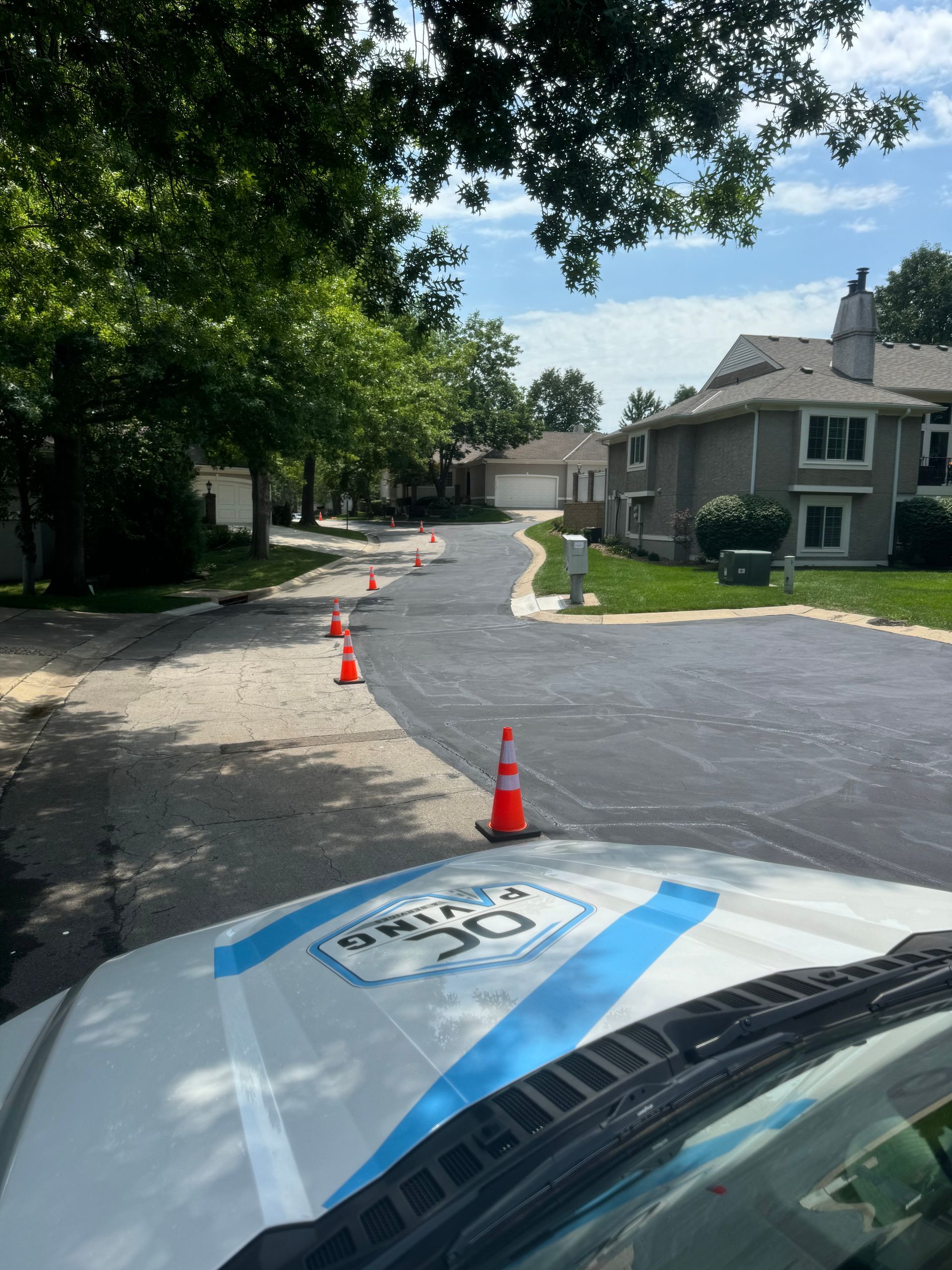 A construction vehicle's hood faces a residential street where traffic cones line the path between asphalt and gravel.