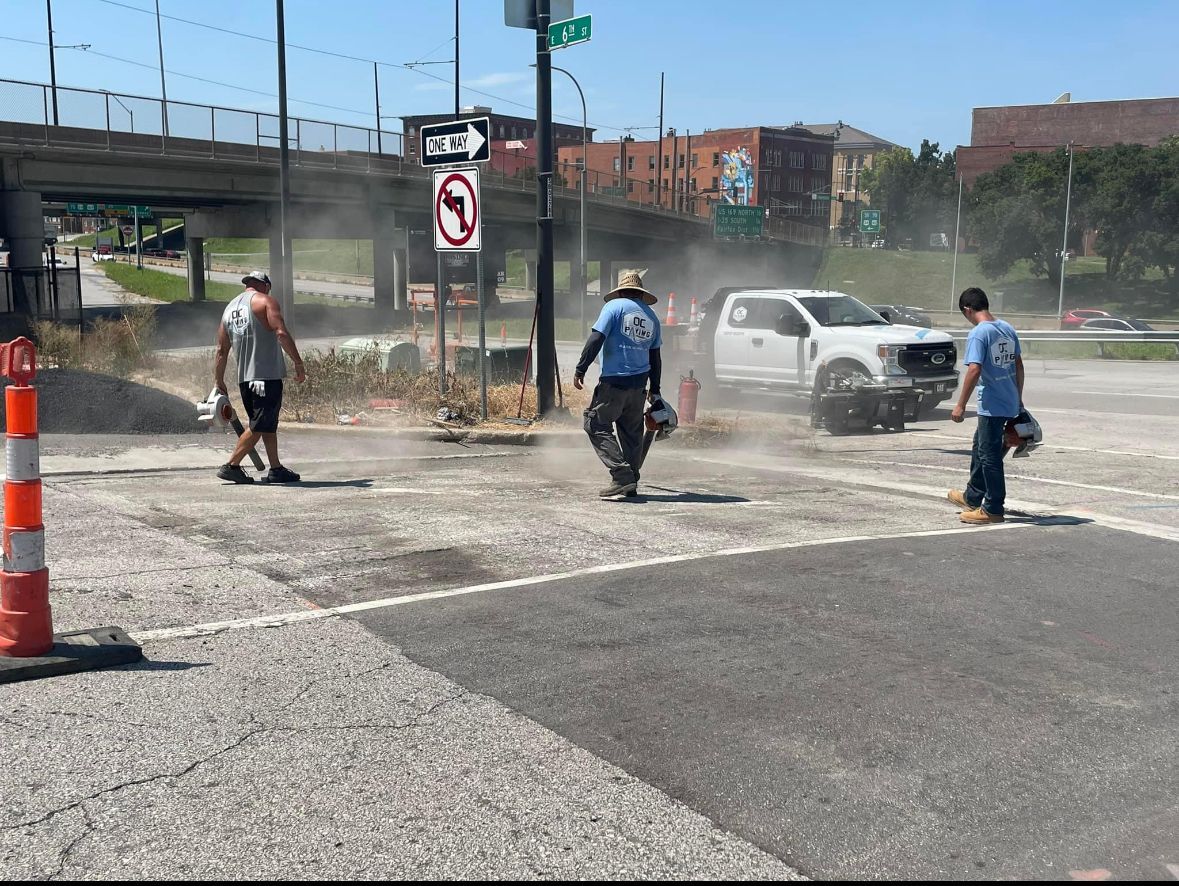 Three workers in high-visibility and casual clothing walk through dust on an urban road near a white pickup truck.