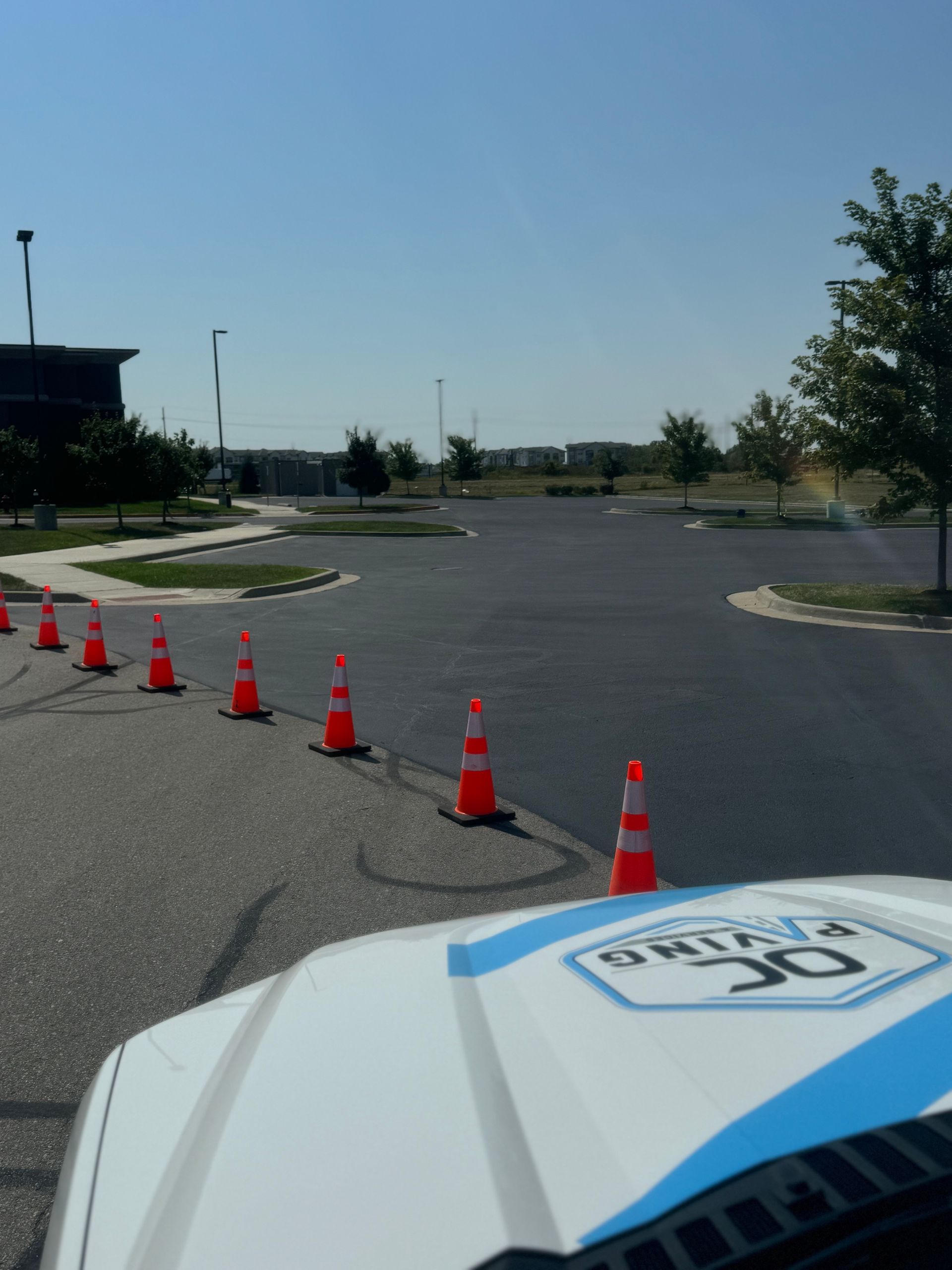 A line of orange traffic cones separates a parking lot from a construction vehicle with paving branding.