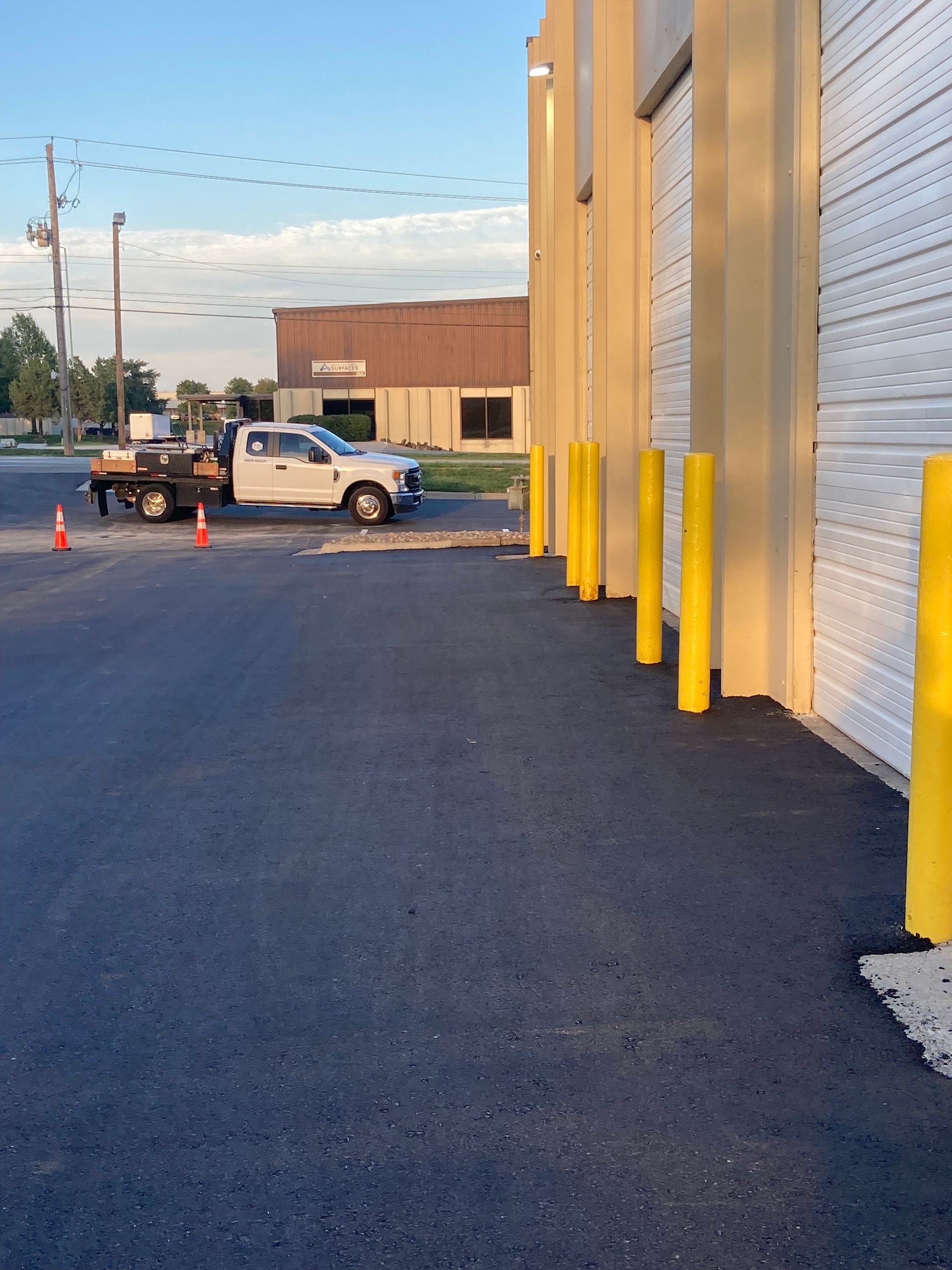 A white utility truck parked outside a warehouse with a row of yellow protective bollards along the building's exterior.