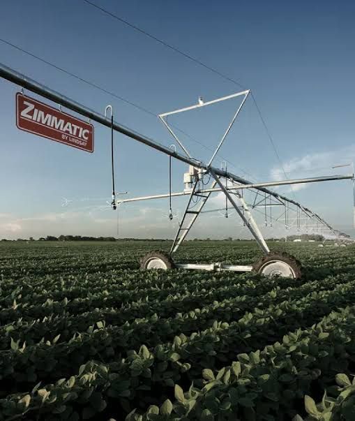Irrigation sprinkler spraying water on a green field with a hillside backdrop.