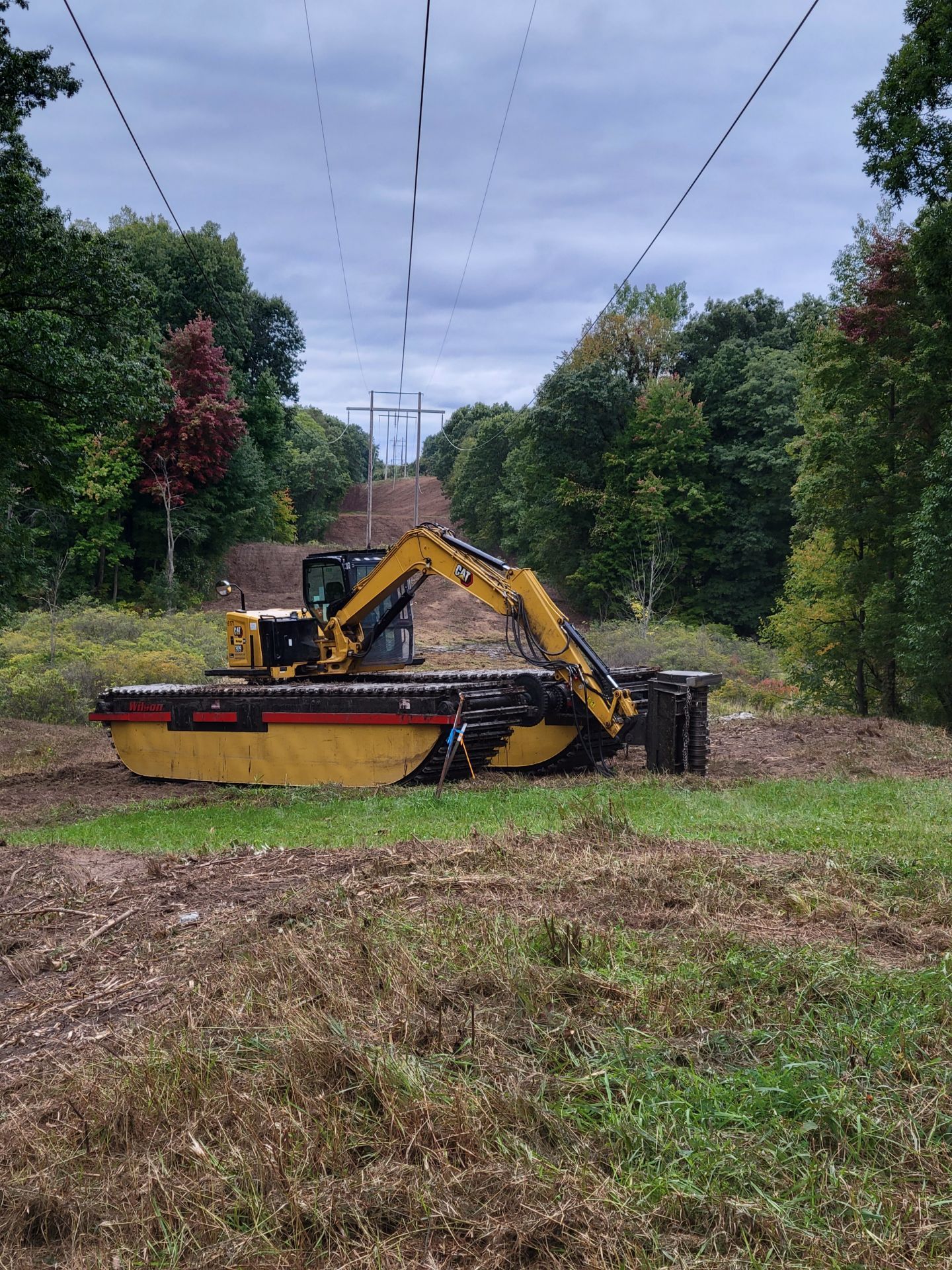 A yellow excavator is sitting in the middle of a grassy field.