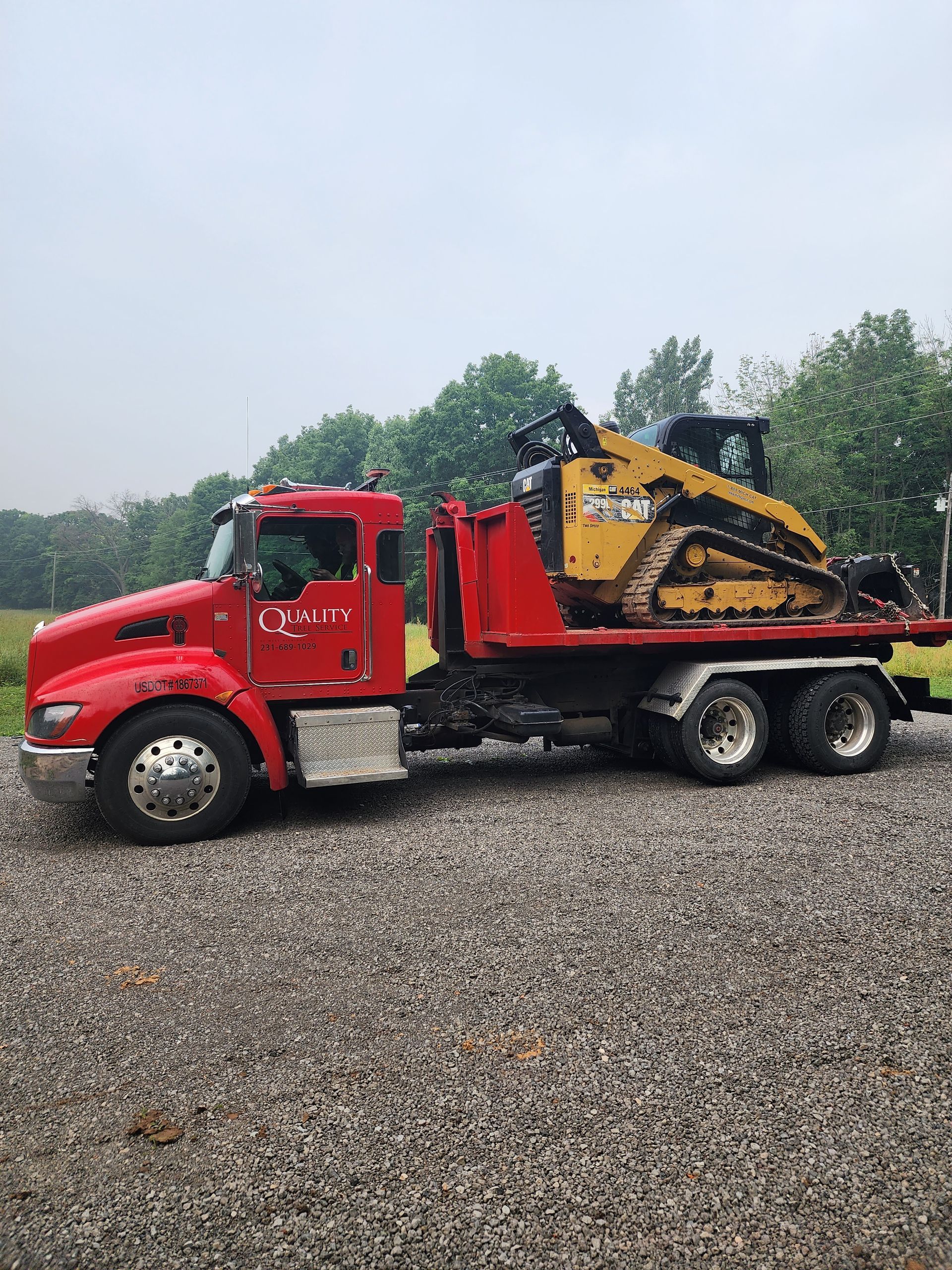 A red truck is towing a yellow bulldozer on a gravel road.