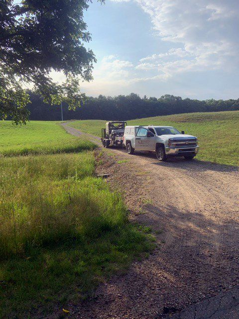 Two trucks are parked on a dirt road in a field