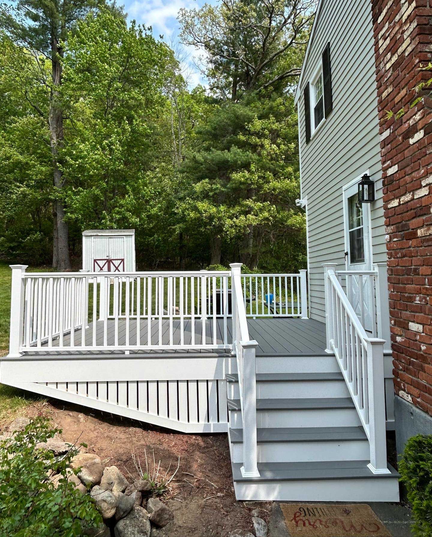 A white deck with stairs leading up to it is next to a brick house.