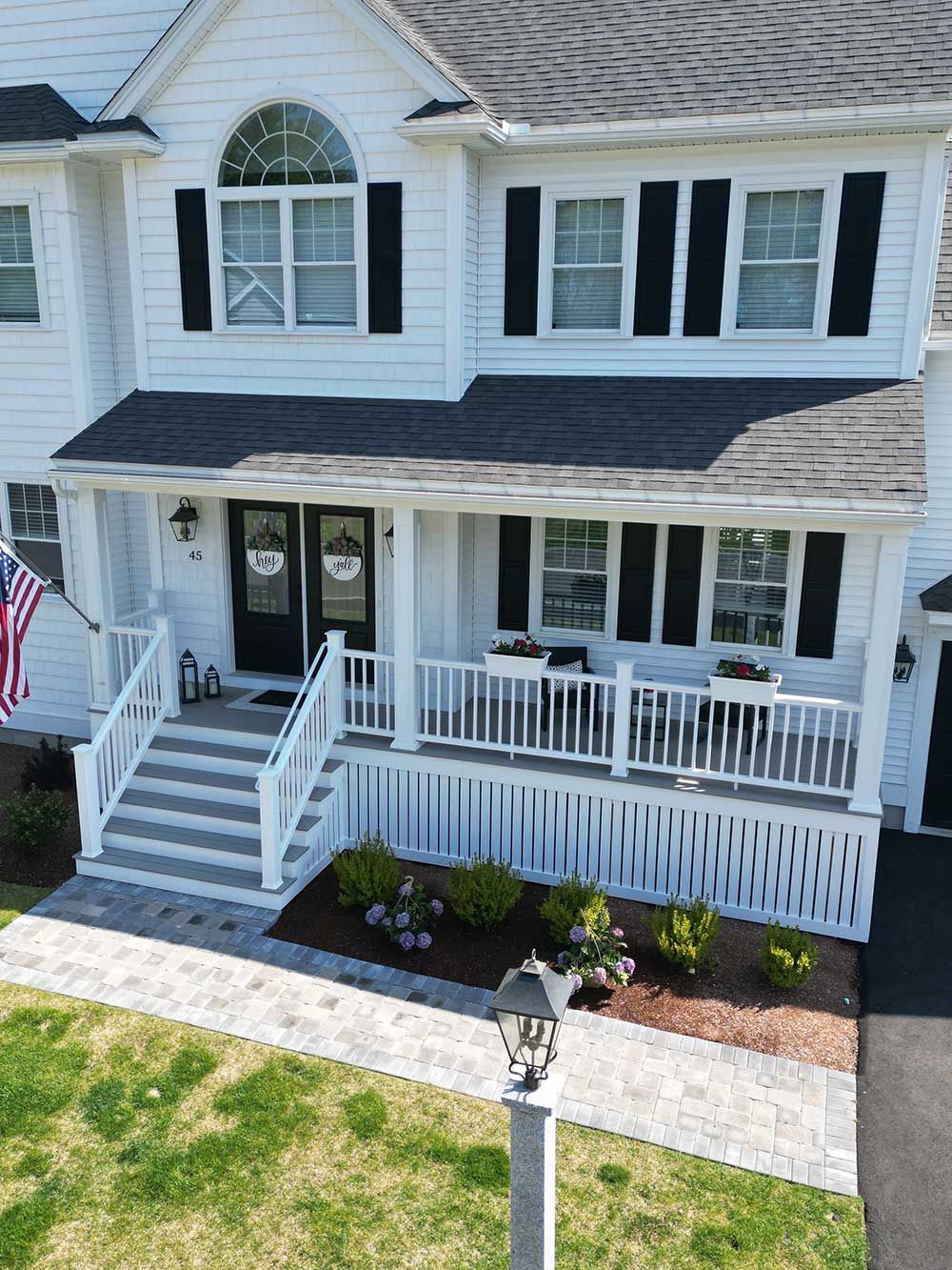 An aerial view of a white house with black shutters and a large porch.