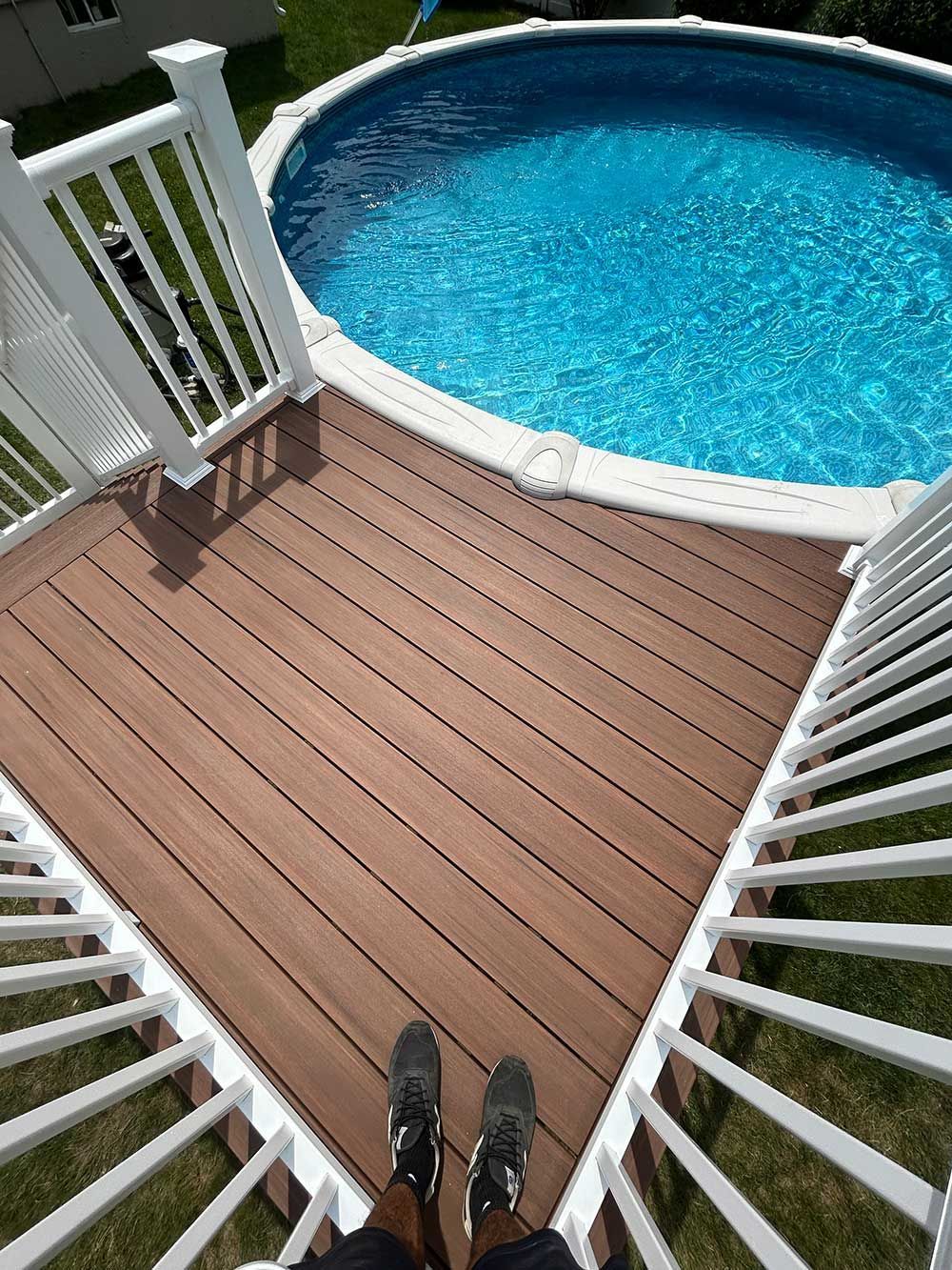 A person is standing on a deck next to a pool.