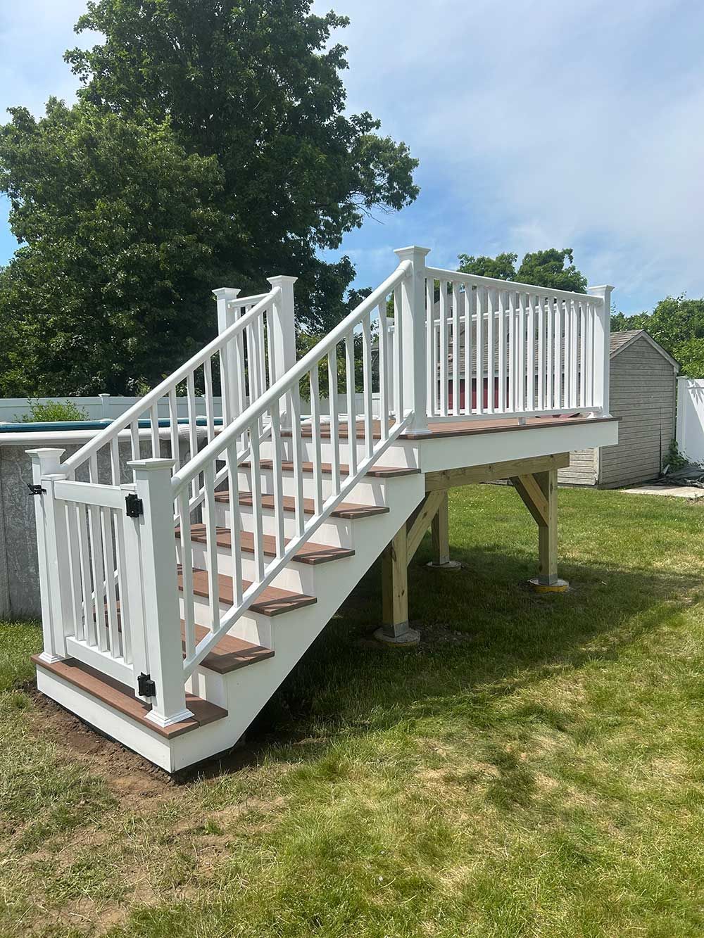 A white deck with stairs leading up to it in a backyard.