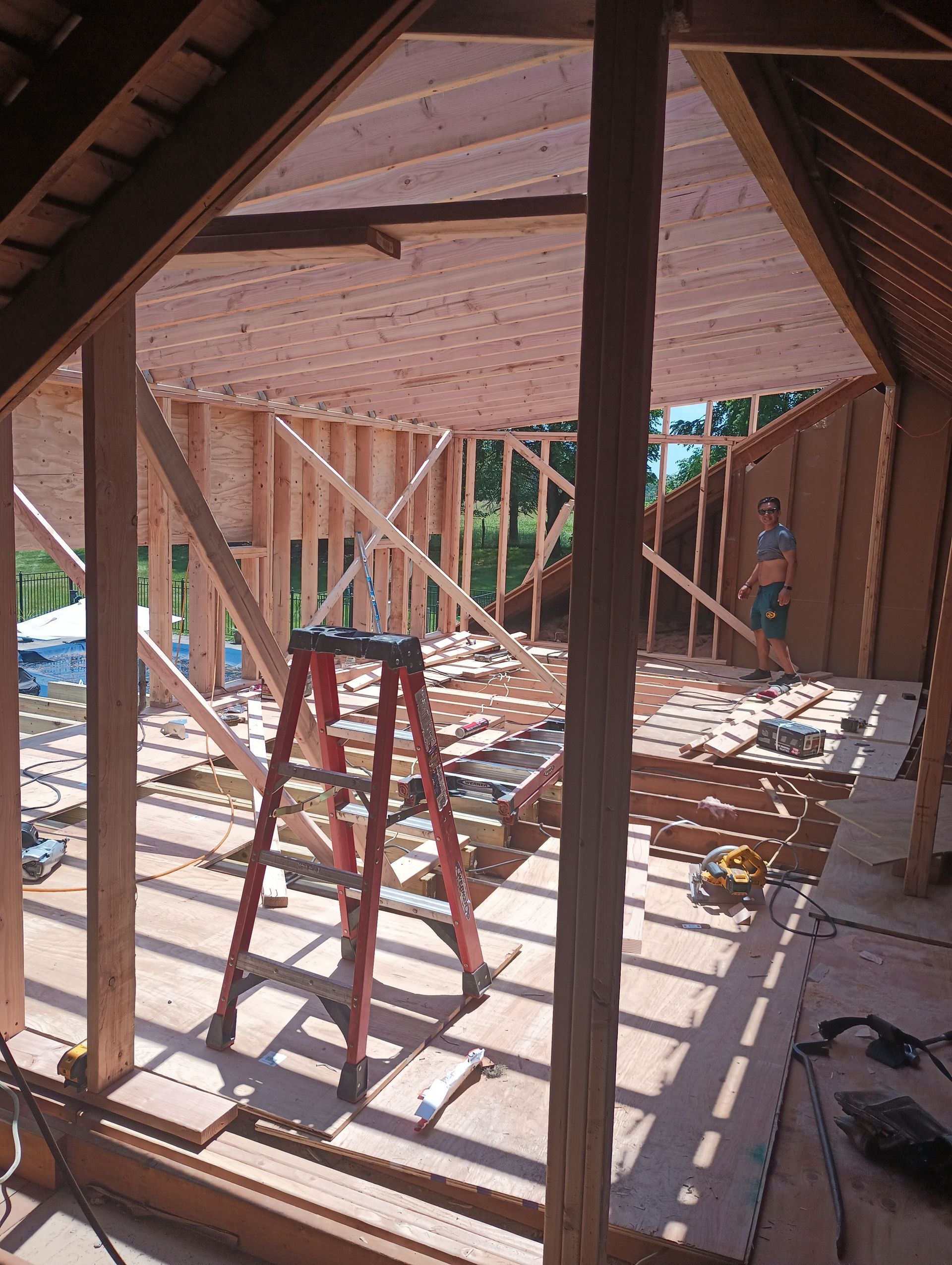 Construction site interior: wooden frame, ladder, visible walls and roof beams, person working.