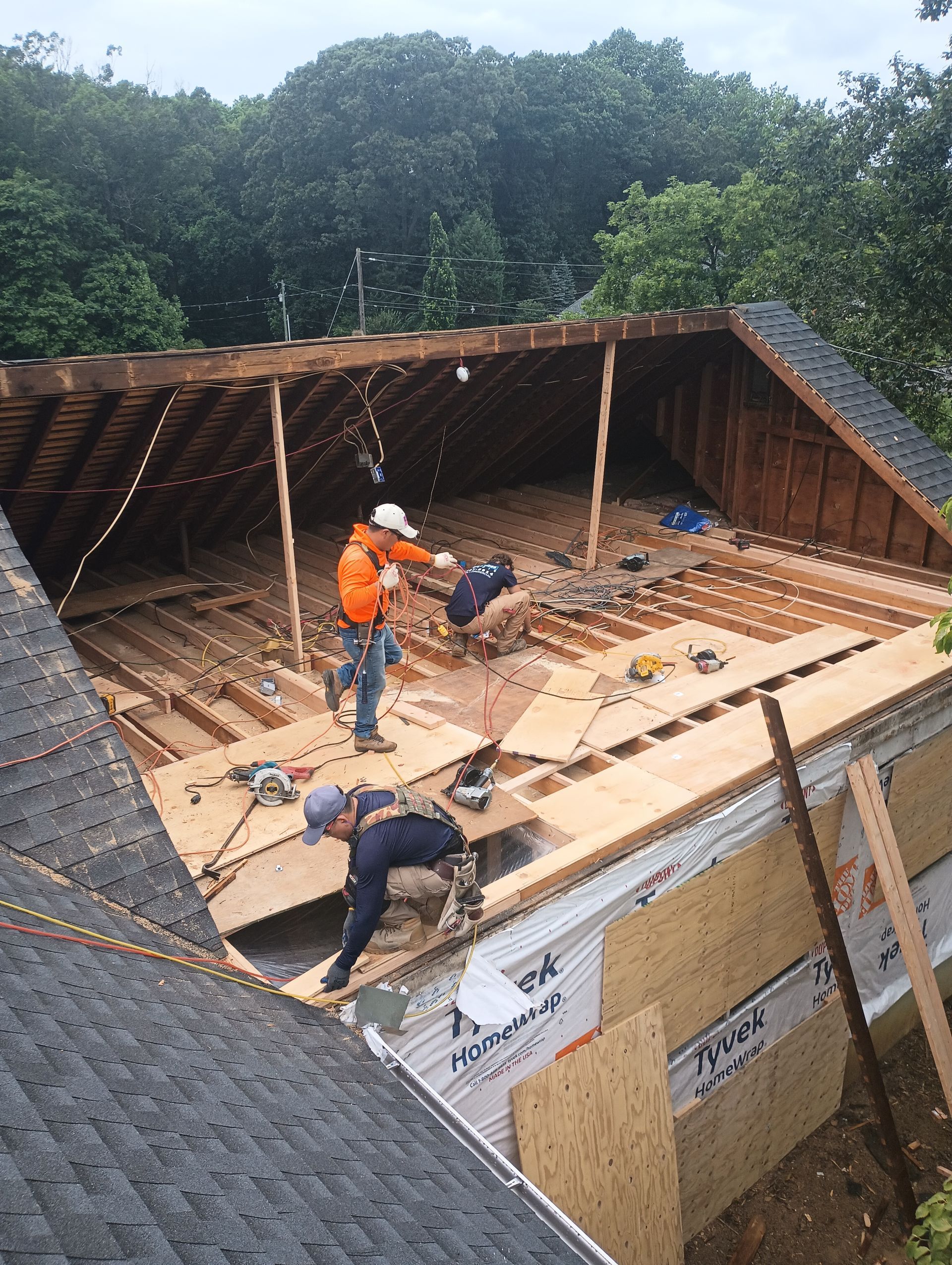 Construction workers renovating a house's roof; removing old wood. Outdoors, sunny.