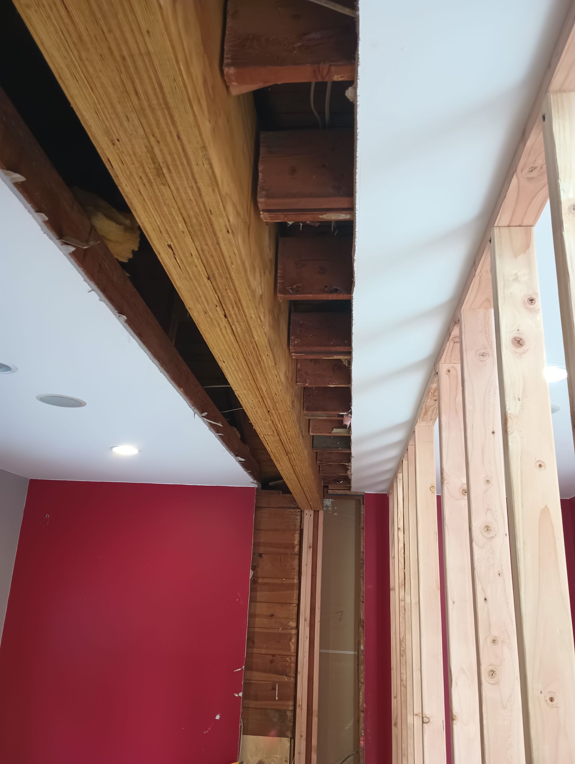 Wooden framework of a wall under construction. Exposed beams and a red wall are visible.
