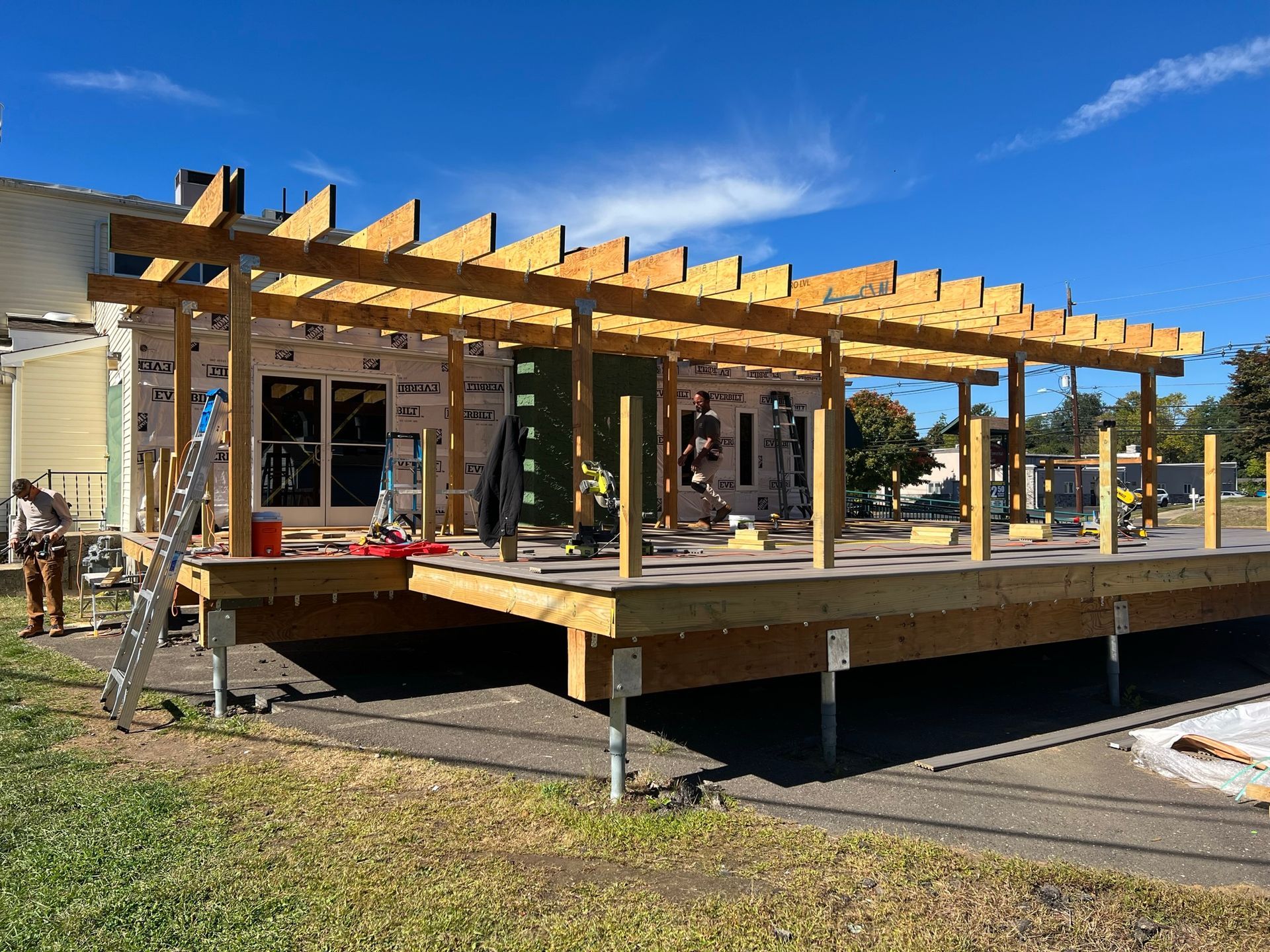 Wooden deck and pergola under construction on a sunny day; person working.
