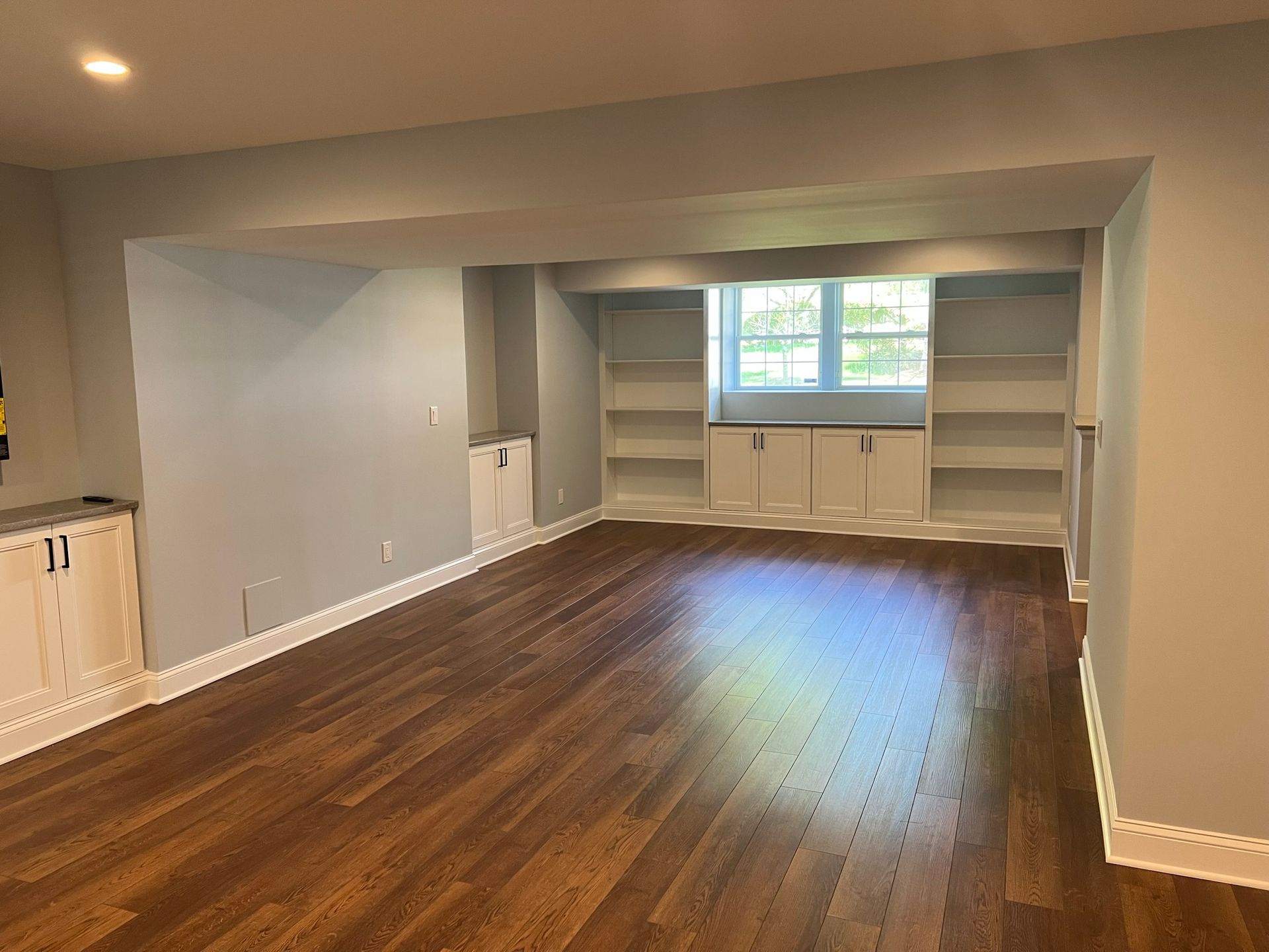 Empty room with hardwood floor, built-in shelves around a window, and gray walls.