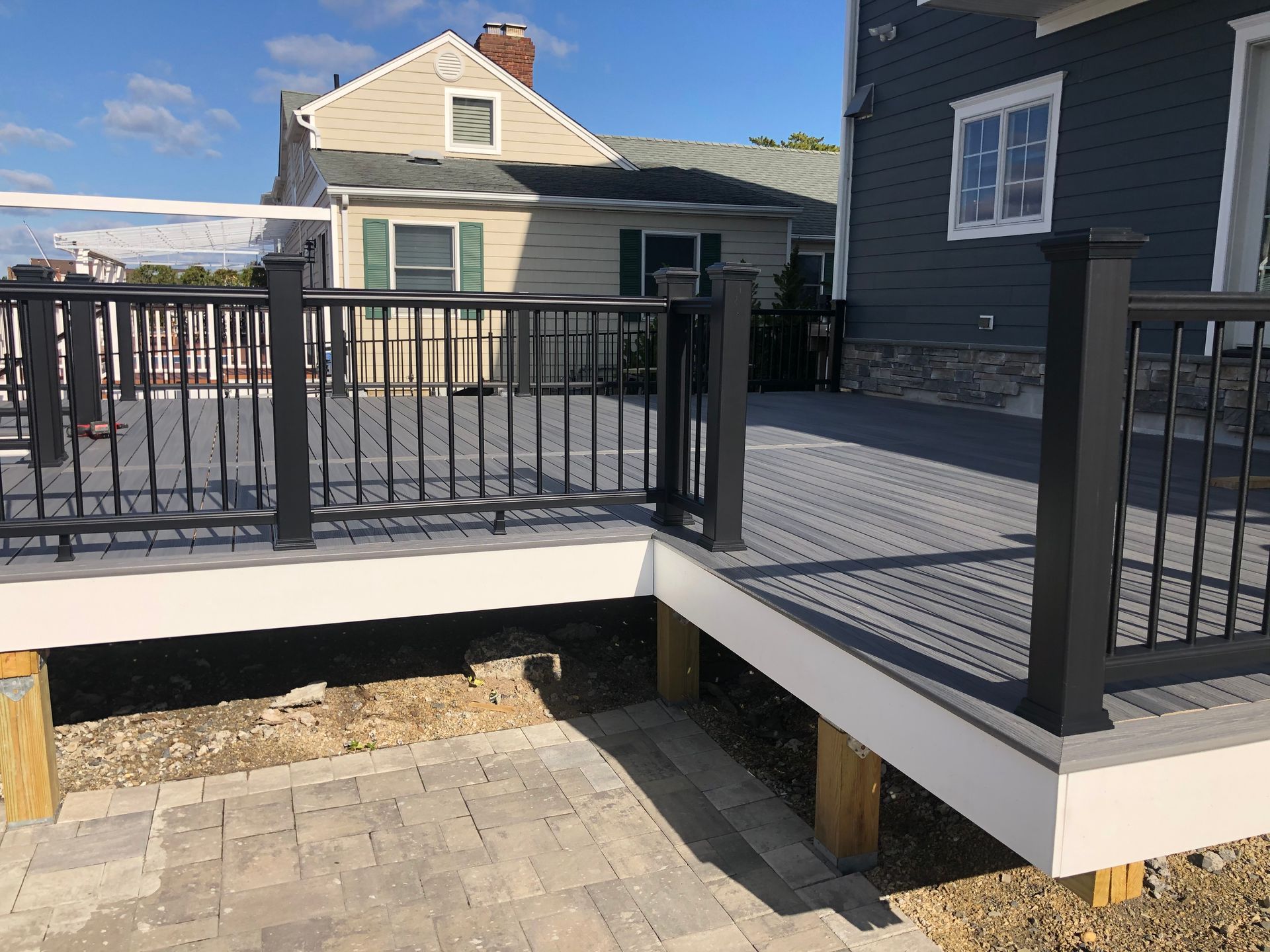 Gray composite deck with black railing and white trim, near a house with a stone patio.