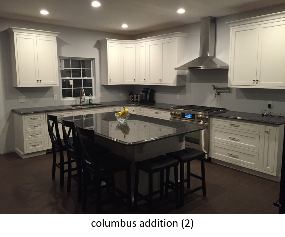 White kitchen cabinets with dark granite countertops, island with stools, stainless steel appliances.