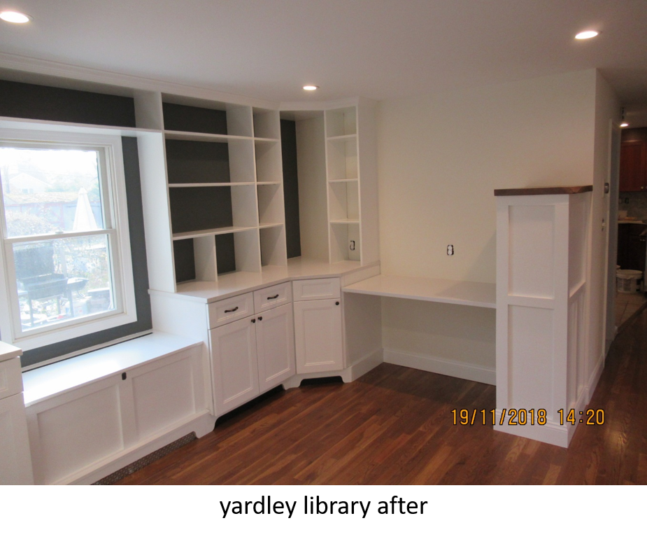 White built-in bookshelves and desk in a room with a window seat, wood floor, and cream-colored walls.