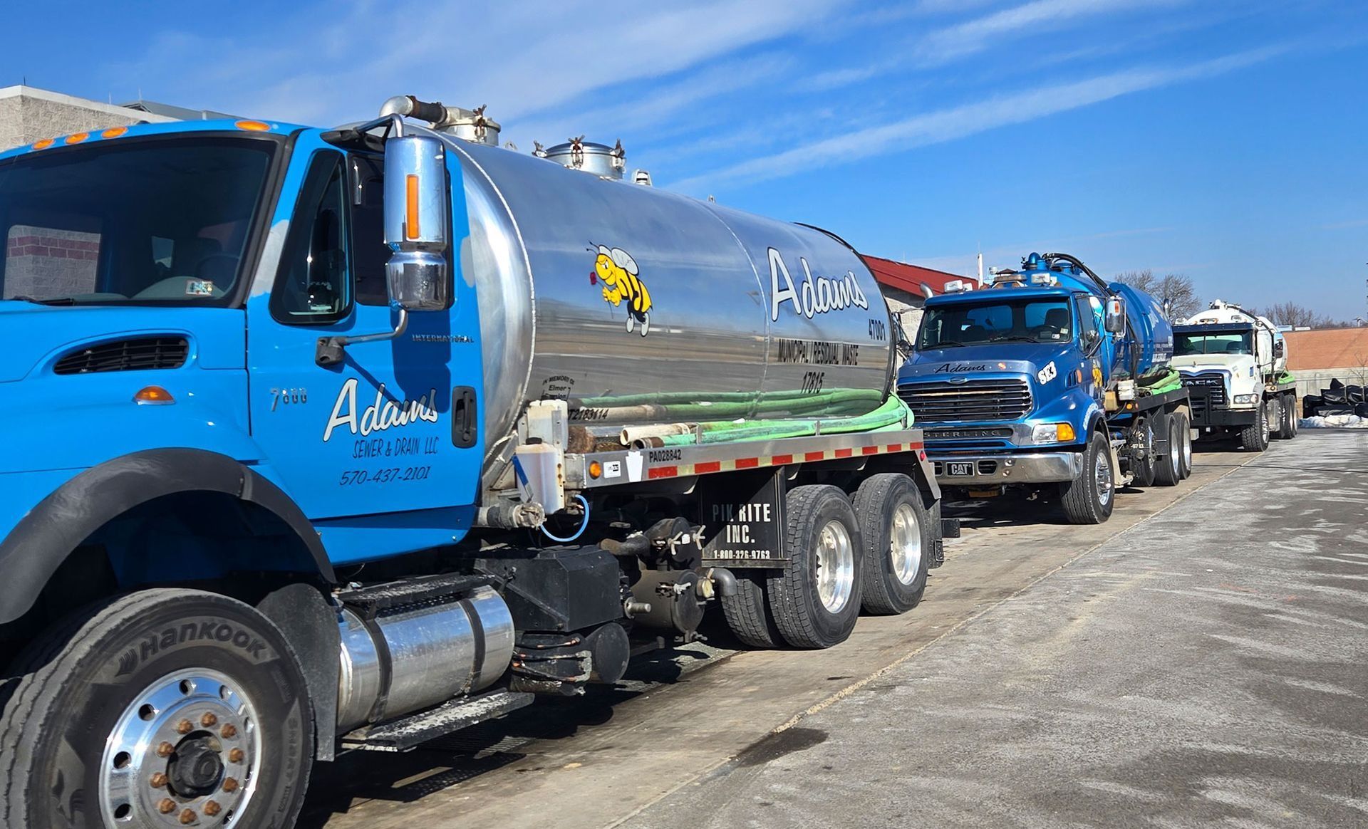 Two workers in blue overalls and yellow gloves vacuuming a septic tank.