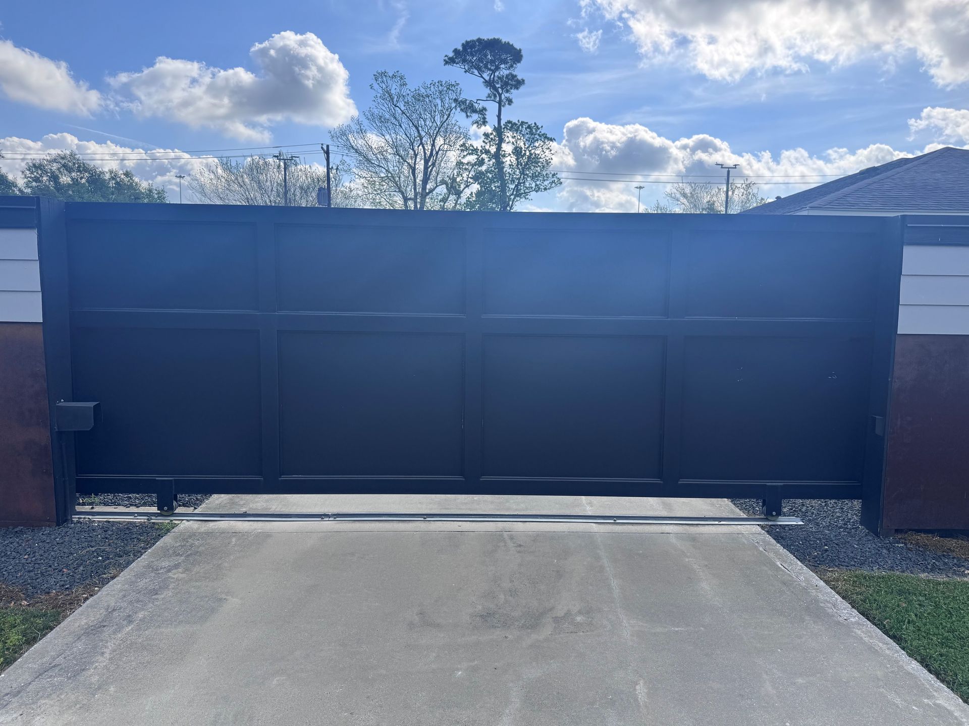 A closed, dark-painted sliding gate with a rectangular panel design, installed across a concrete residential driveway.