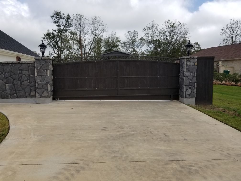 Dark brown automatic gate between stone pillars, set on a concrete driveway.