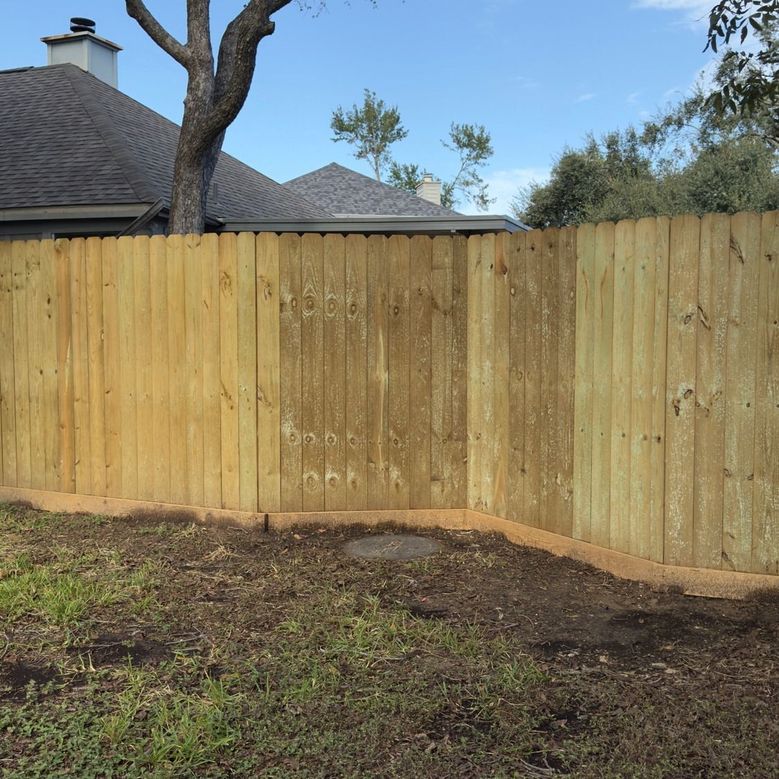 Wooden fence bordering a yard, with visible weathering and a house in the background under a blue sky.