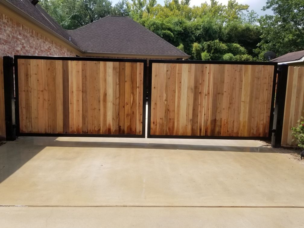 Wooden driveway gate, two panels, with black metal frame, on concrete surface.