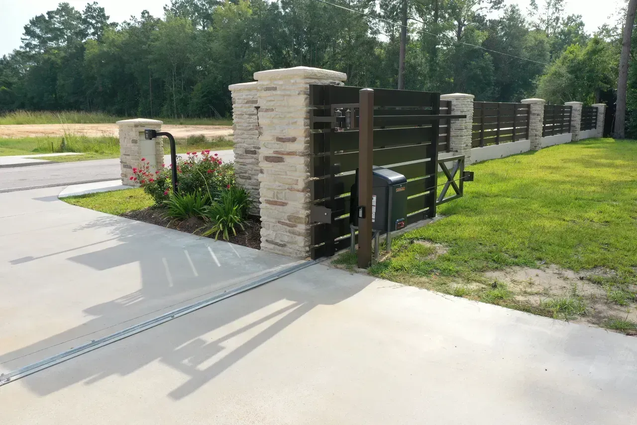 Entrance gate with stone pillars, black wooden gate, and a concrete driveway.