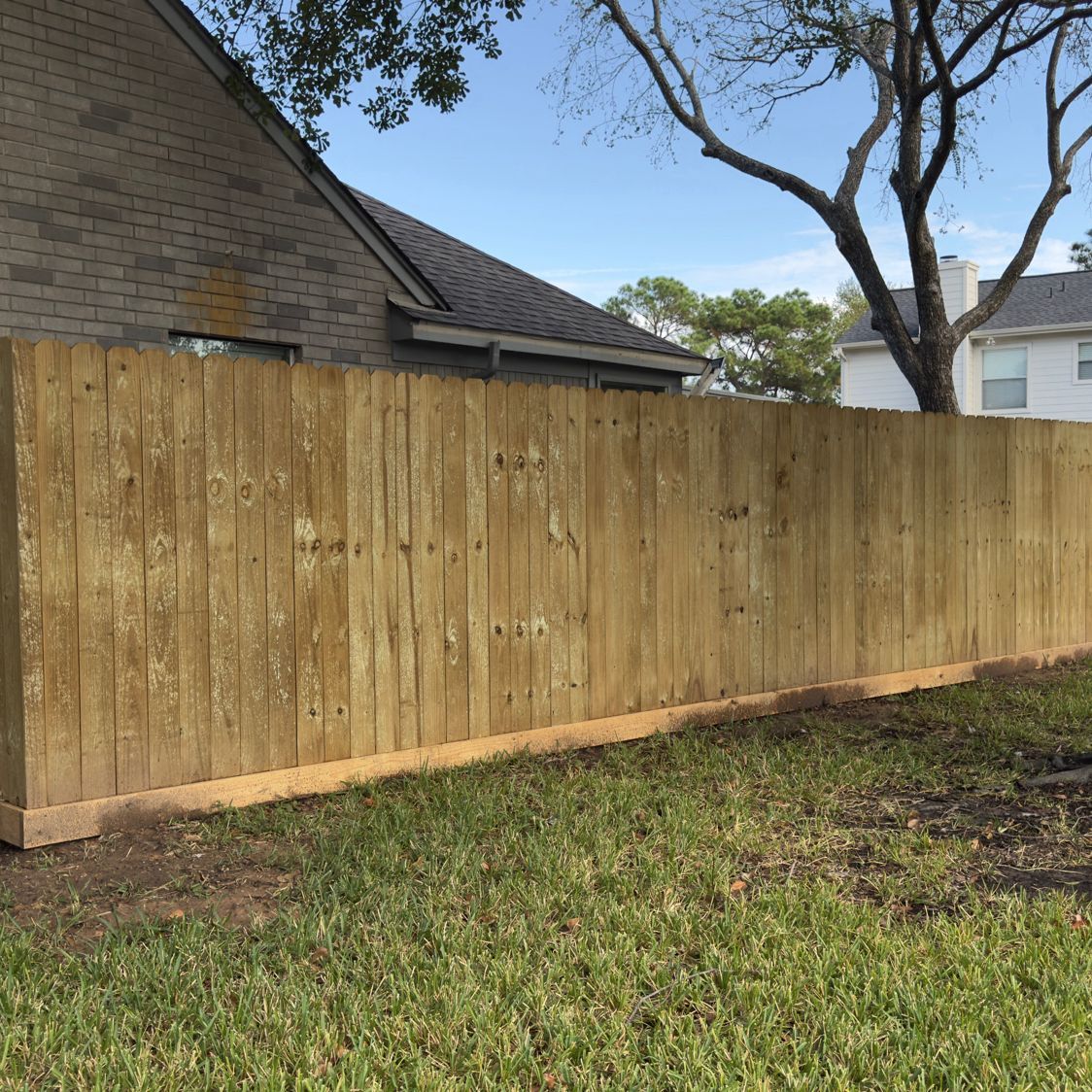 Wooden fence in backyard, next to a brick house and green grass.