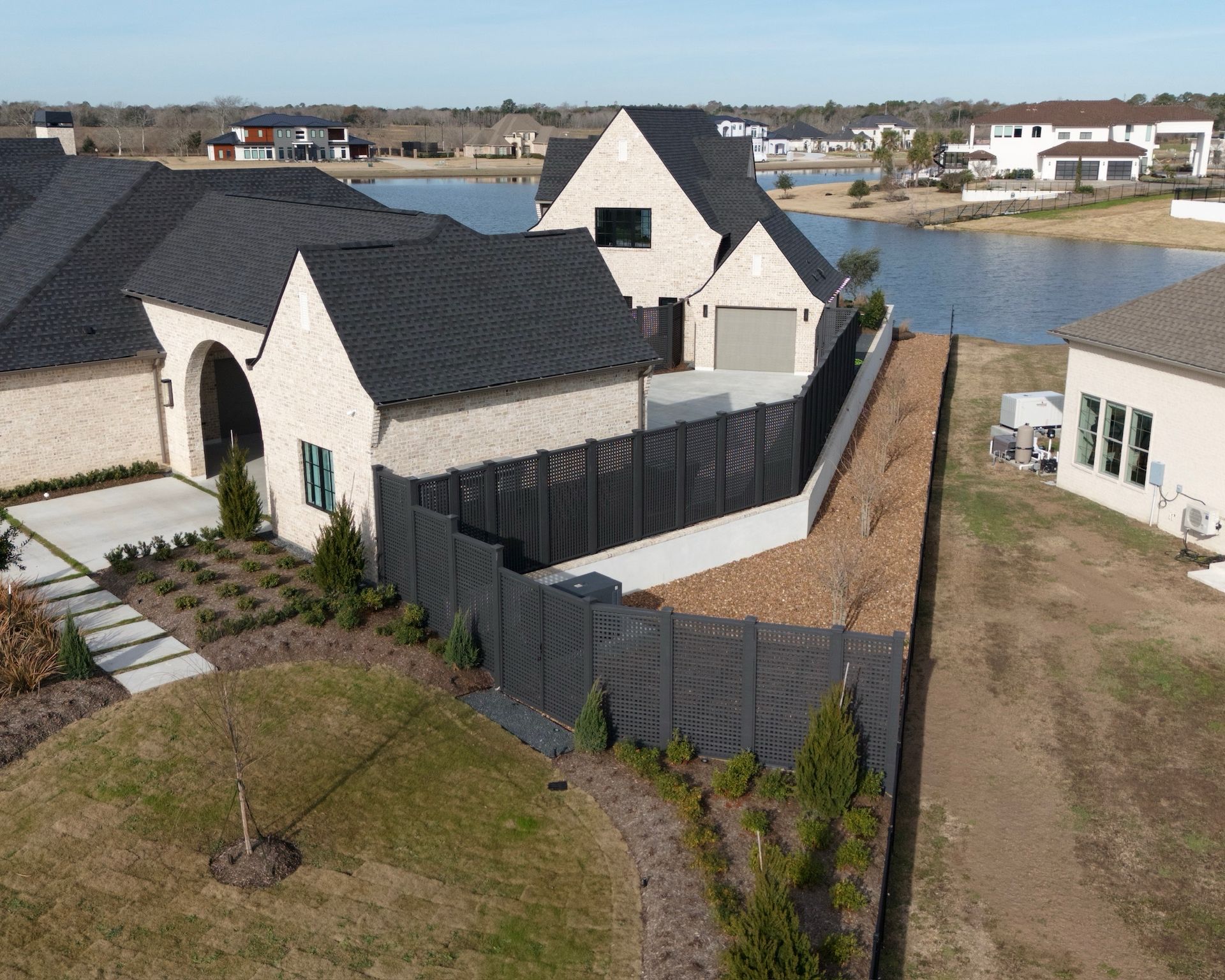 A two-story home with a black fence sits near a lake on a sunny day.