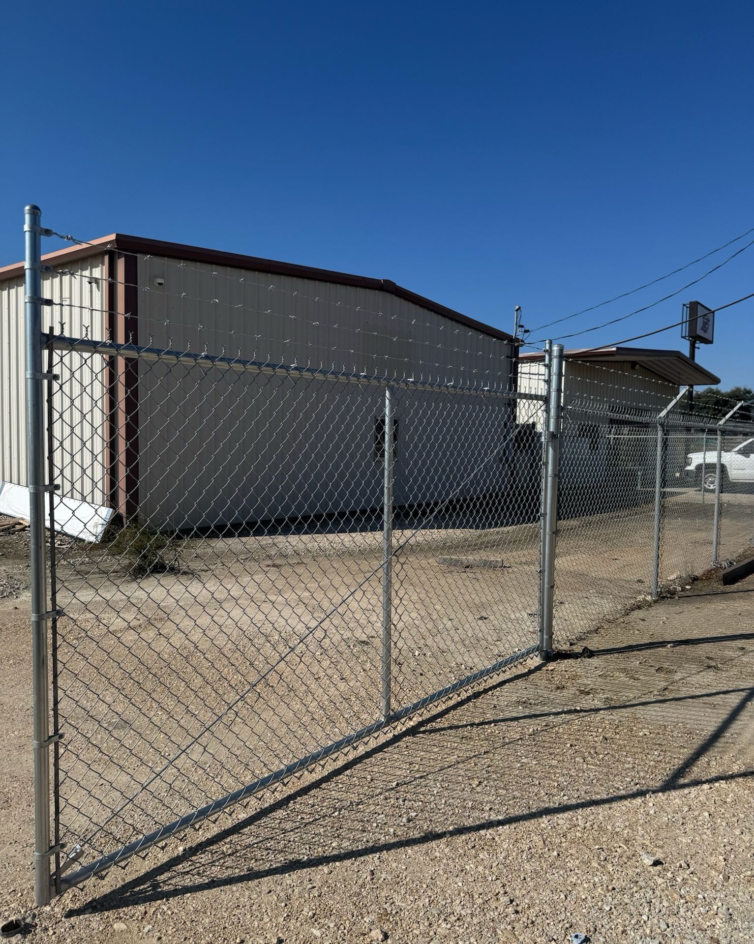 Chain-link fence surrounding a beige building, topped with barbed wire, under a clear blue sky.