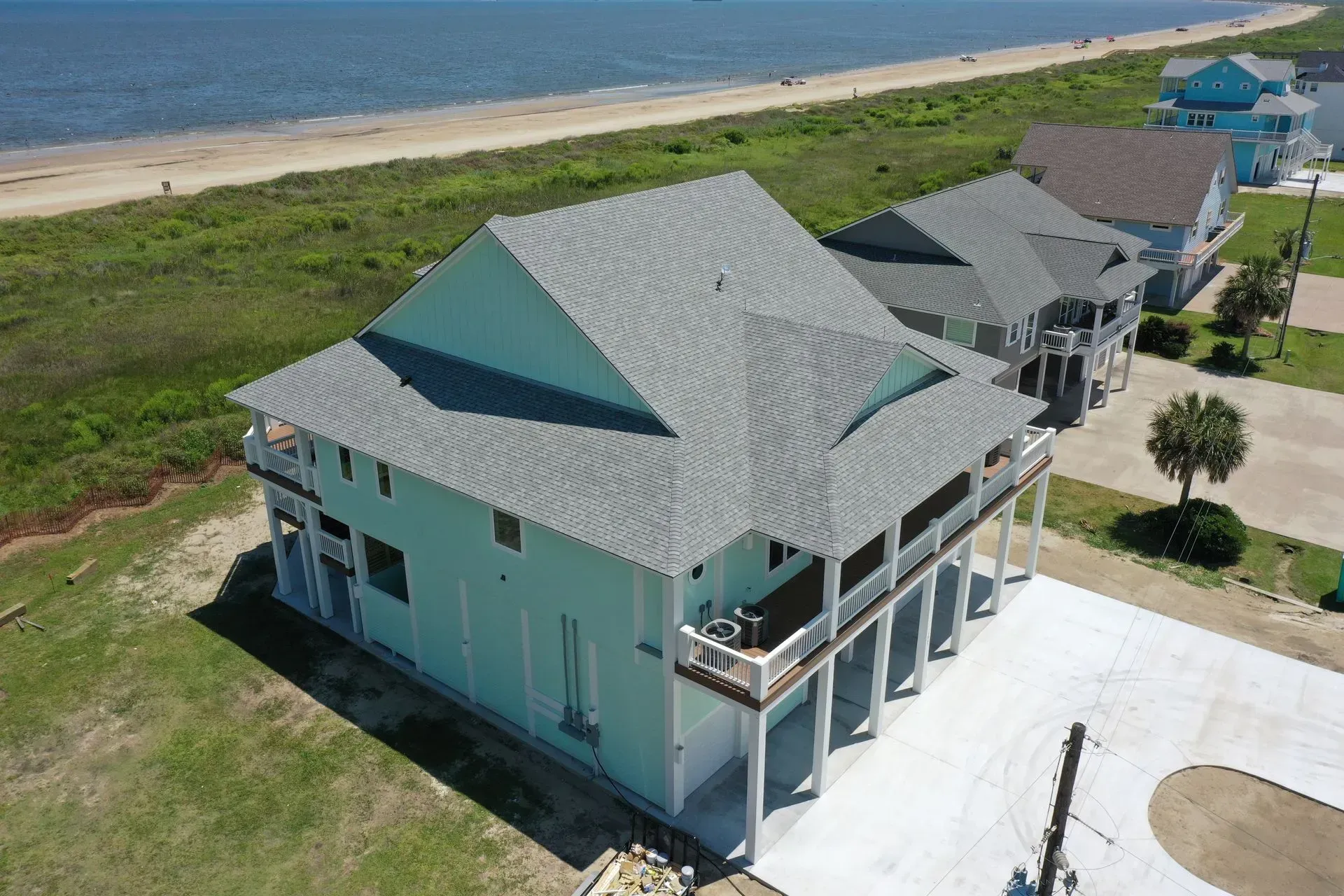Light blue beach house with grey roof and porch overlooking a beach with ocean.