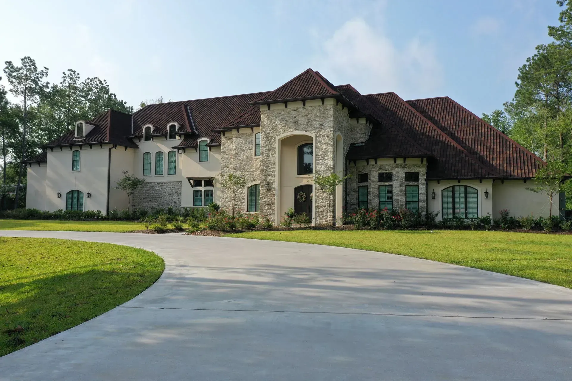 Luxurious stone and stucco mansion with a red tile roof and long driveway.