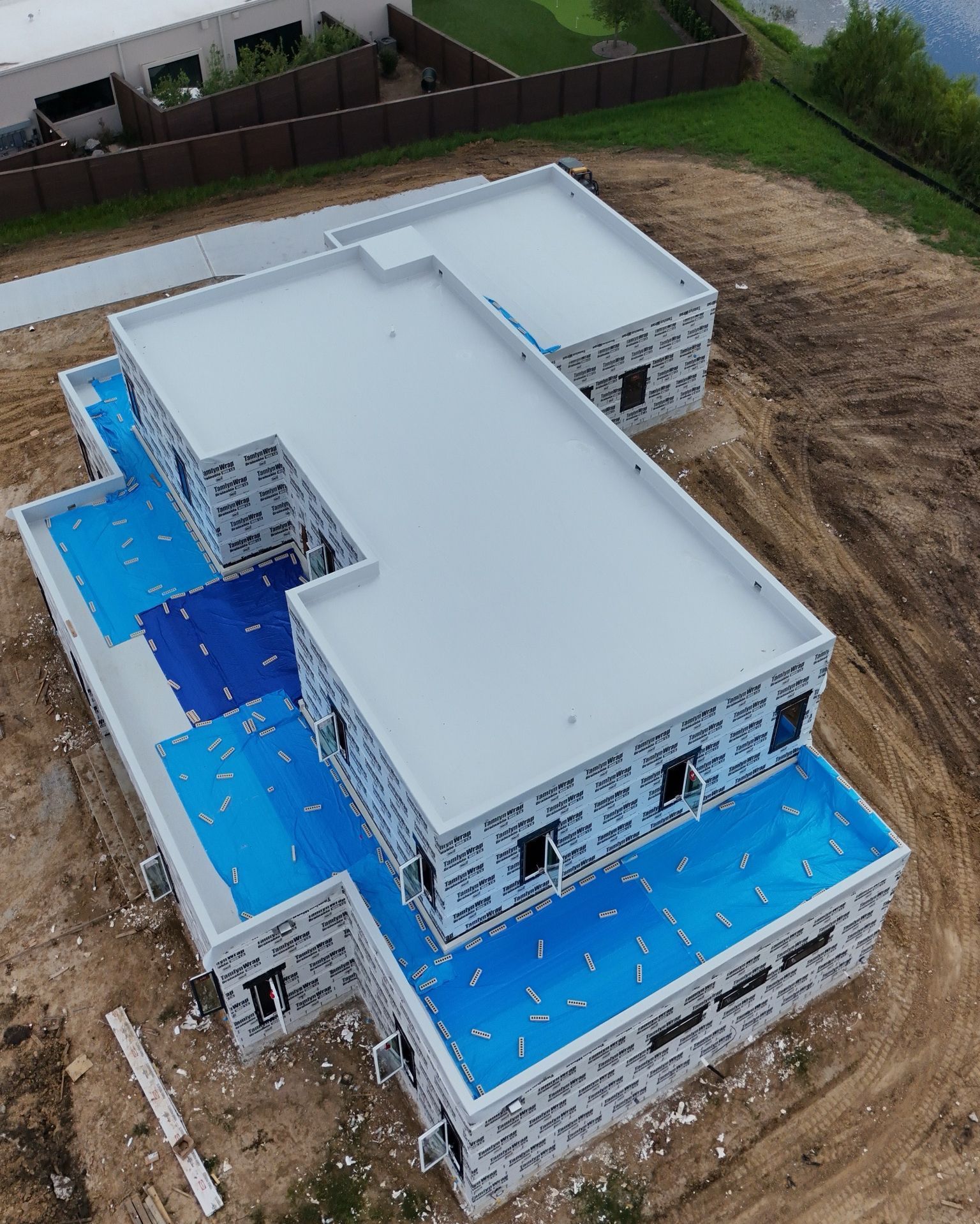 Aerial view of a building under construction. White walls, blue roofing material, on a dirt lot.