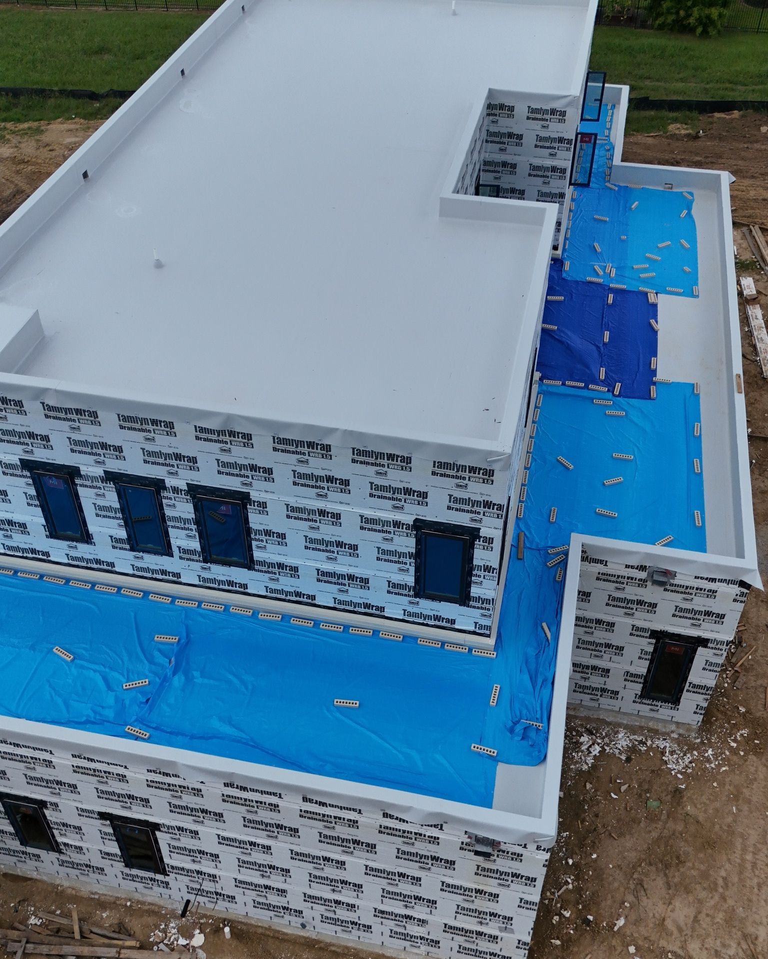 A multi-level building under construction with flat, white roofs and blue protective coverings.