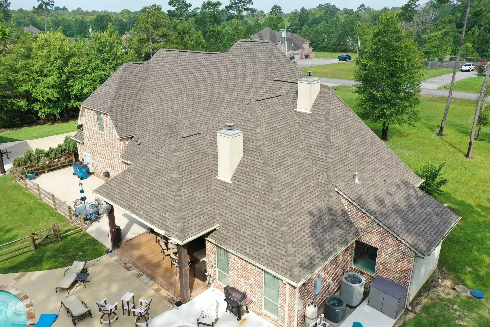 A two-story brick house with a brown shingle roof, chimney, and a backyard with a pool.