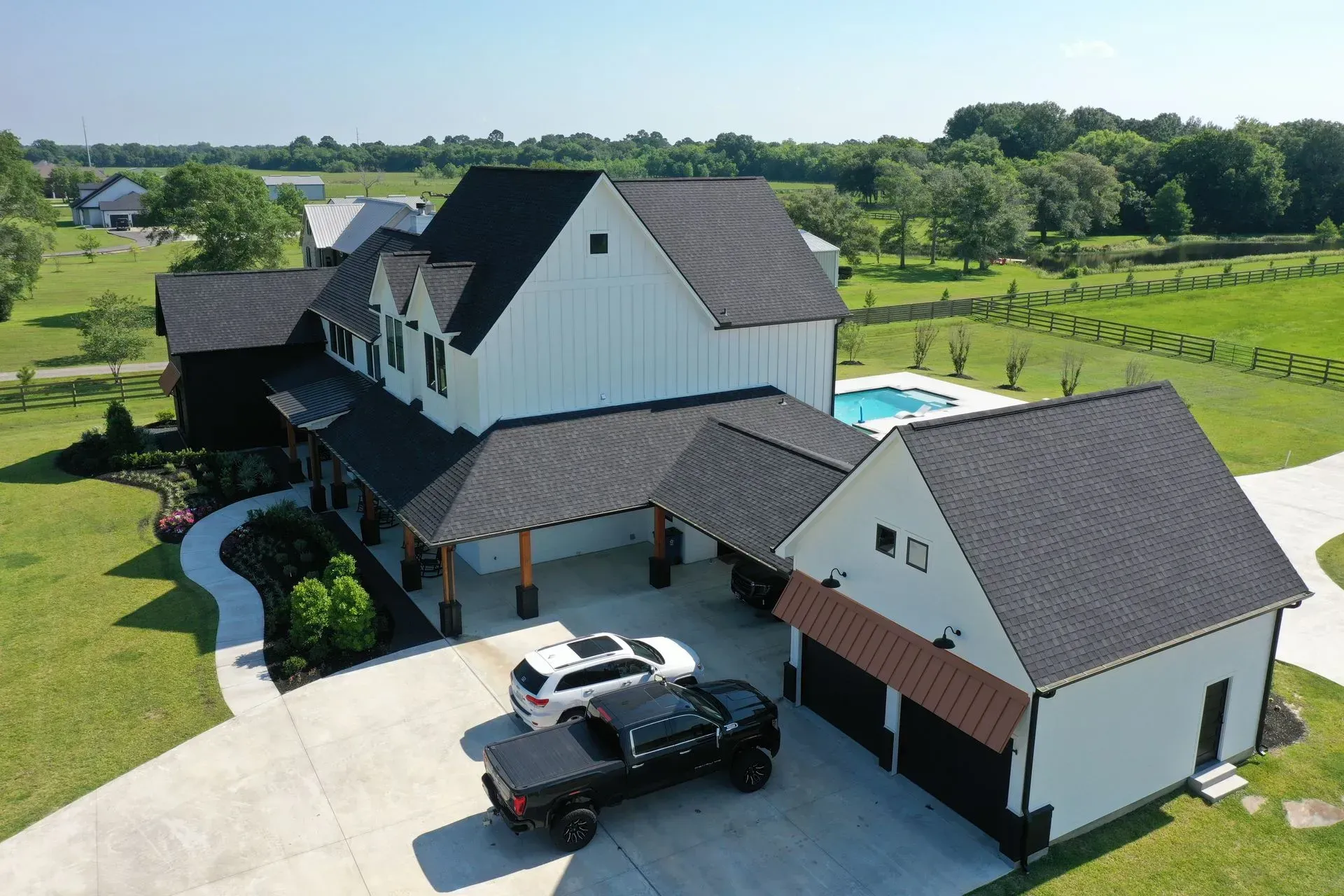 Modern farmhouse with black roof, white siding, pool, and cars in the driveway.