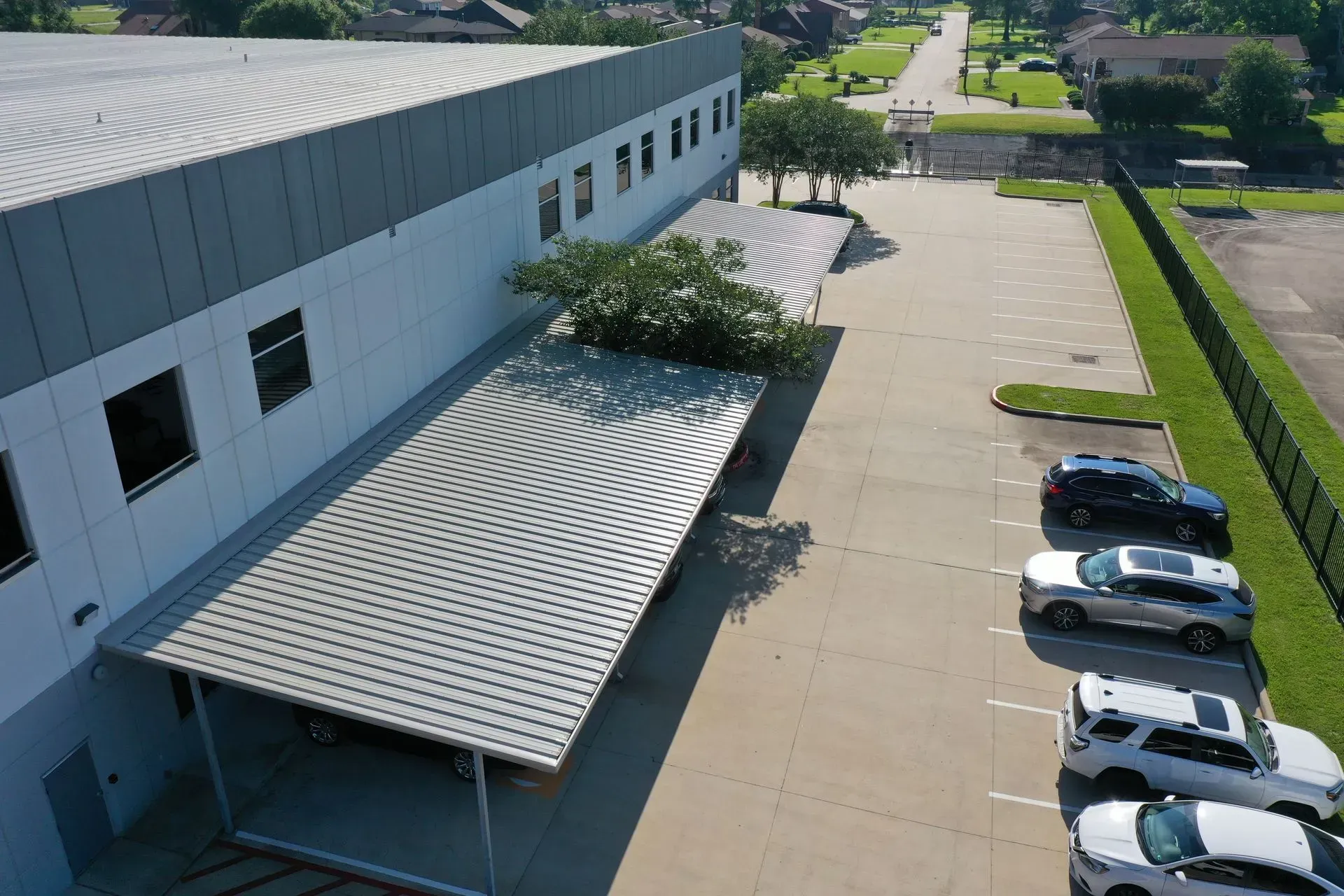 A modern building with a curved metal awning, a parking lot with vehicles, and a view of a residential street.