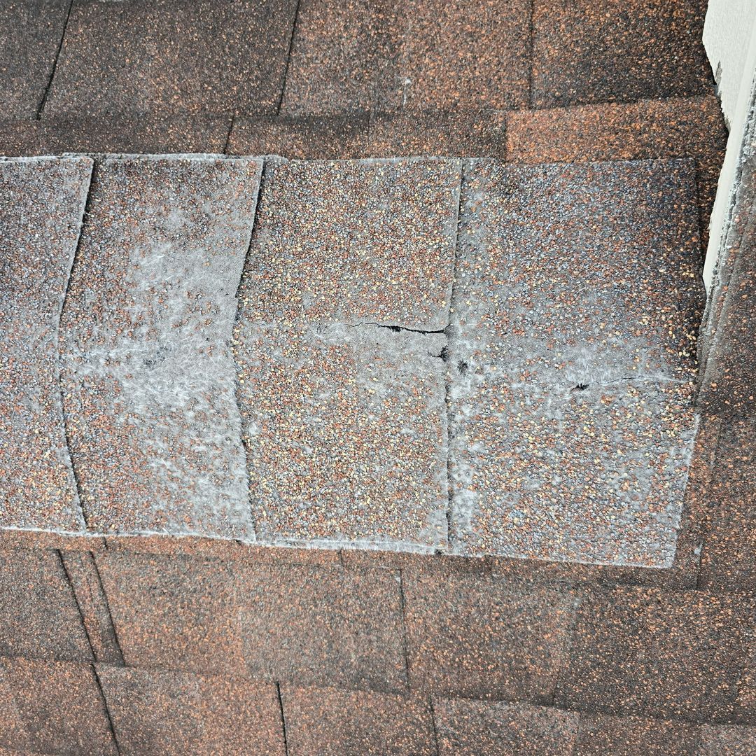 Close-up of brown asphalt roof shingles with light-colored streaks and small cracks.