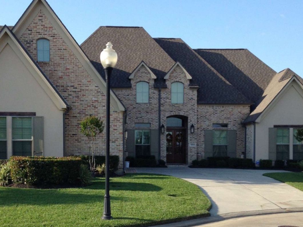 Large brick house with a brown roof, green shutters, and a black lamp post on a sunny day.
