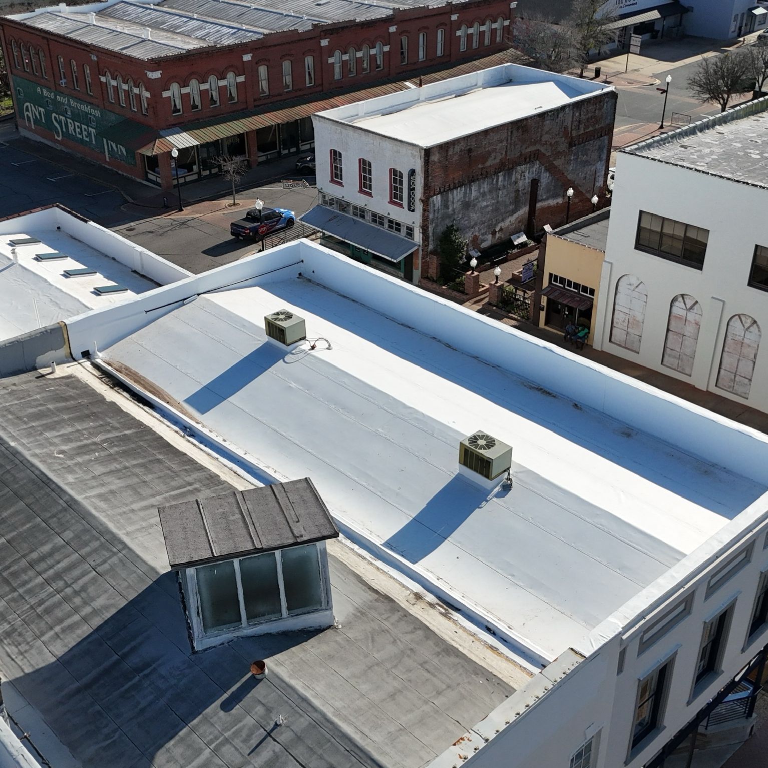 Aerial view of buildings with white flat roofs, including AC units, in a town setting.