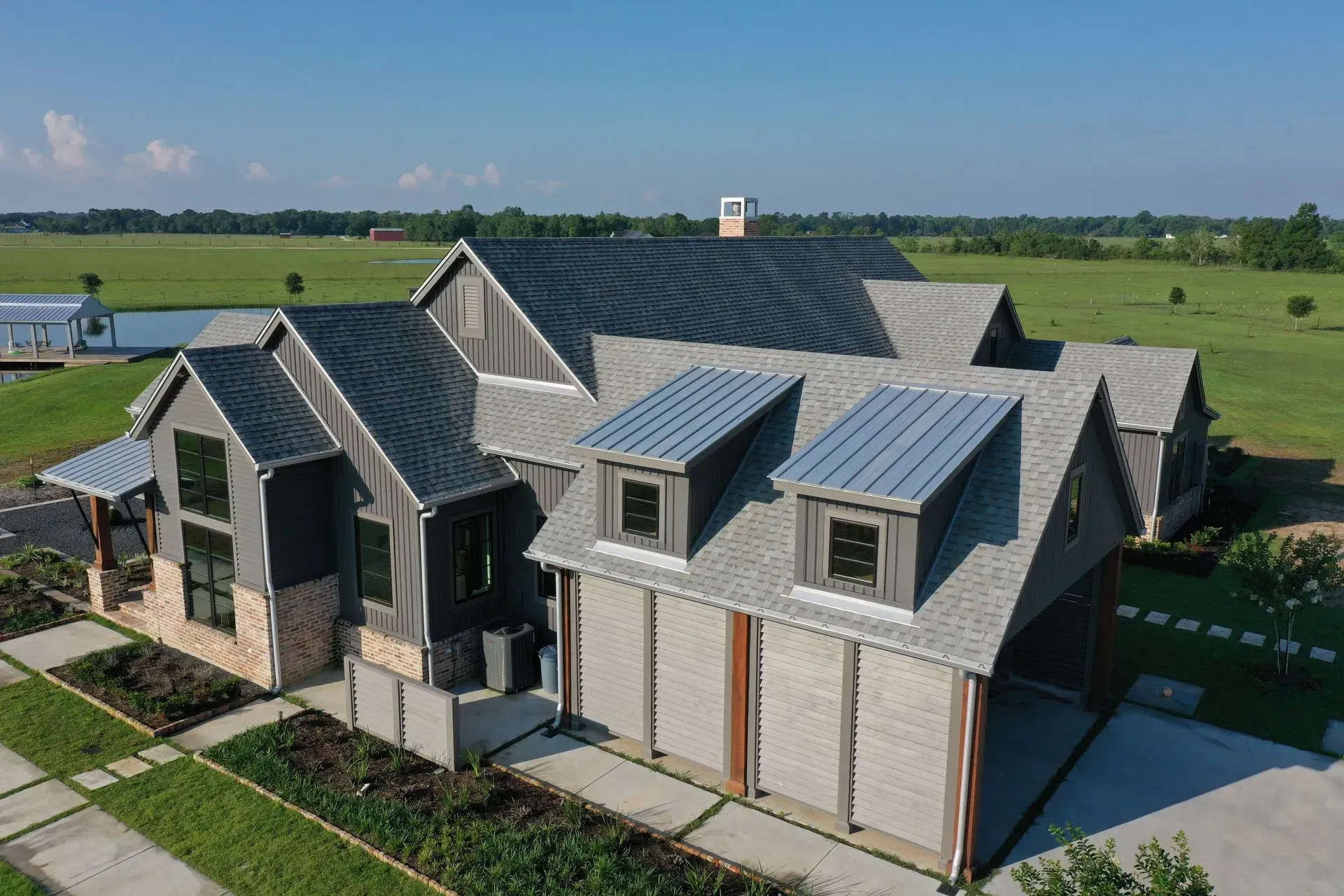Modern farmhouse with grey siding and metal roof on a green field under a blue sky.