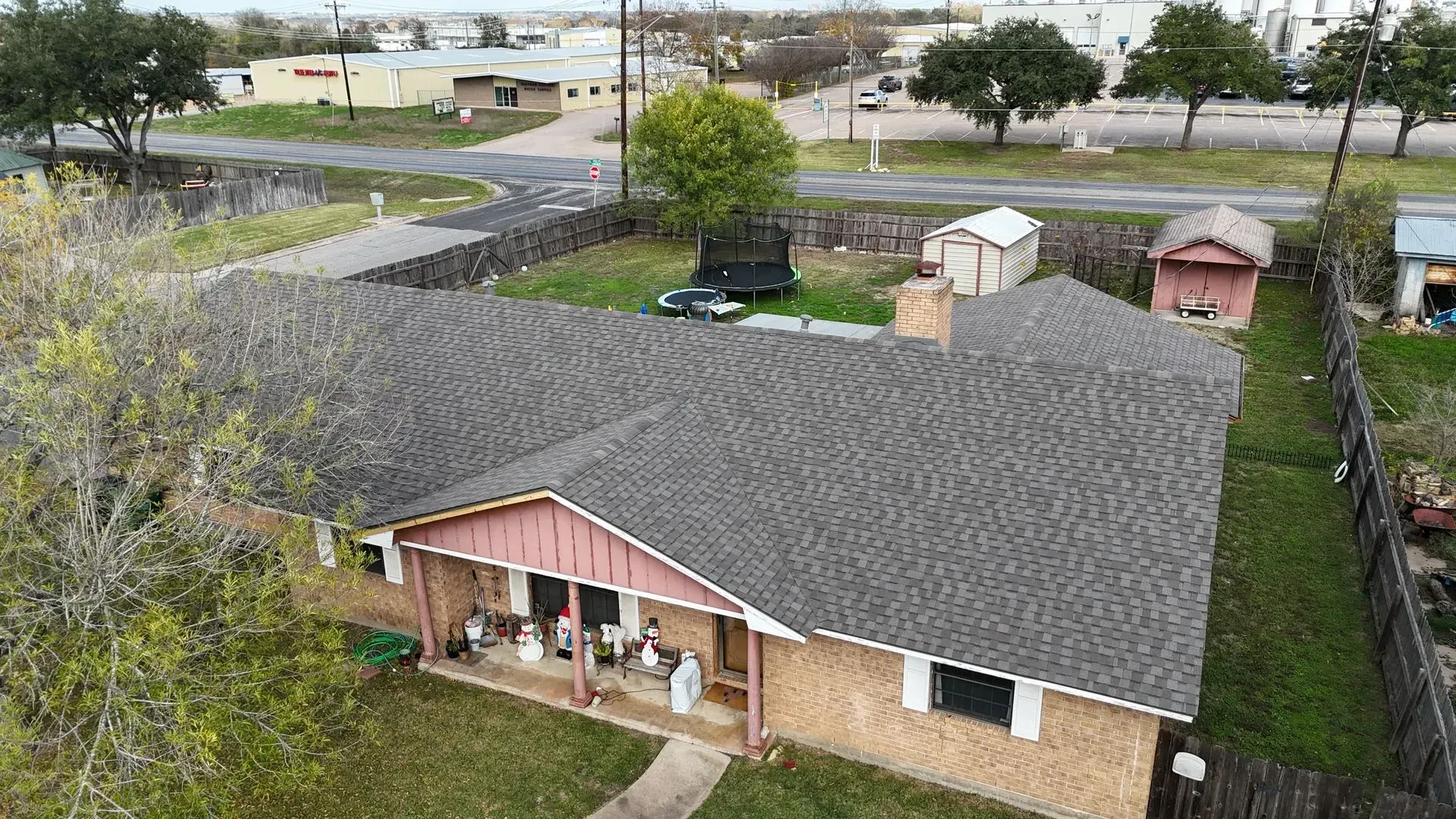 Overhead view of a one-story brick house with a dark roof and small yard surrounded by a wooden fence.