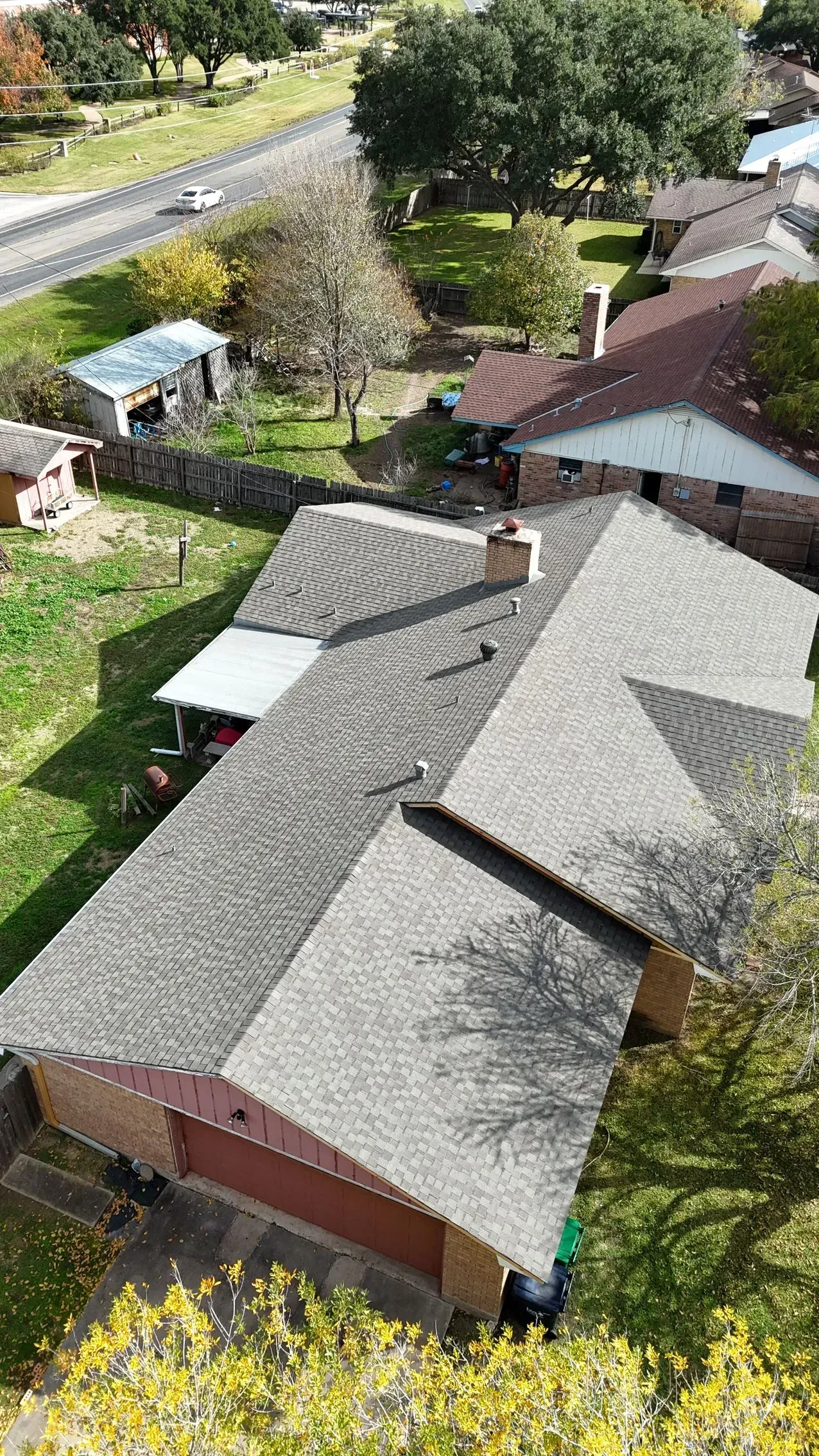 Overhead view of a house with a gray shingled roof, trees, and a road.