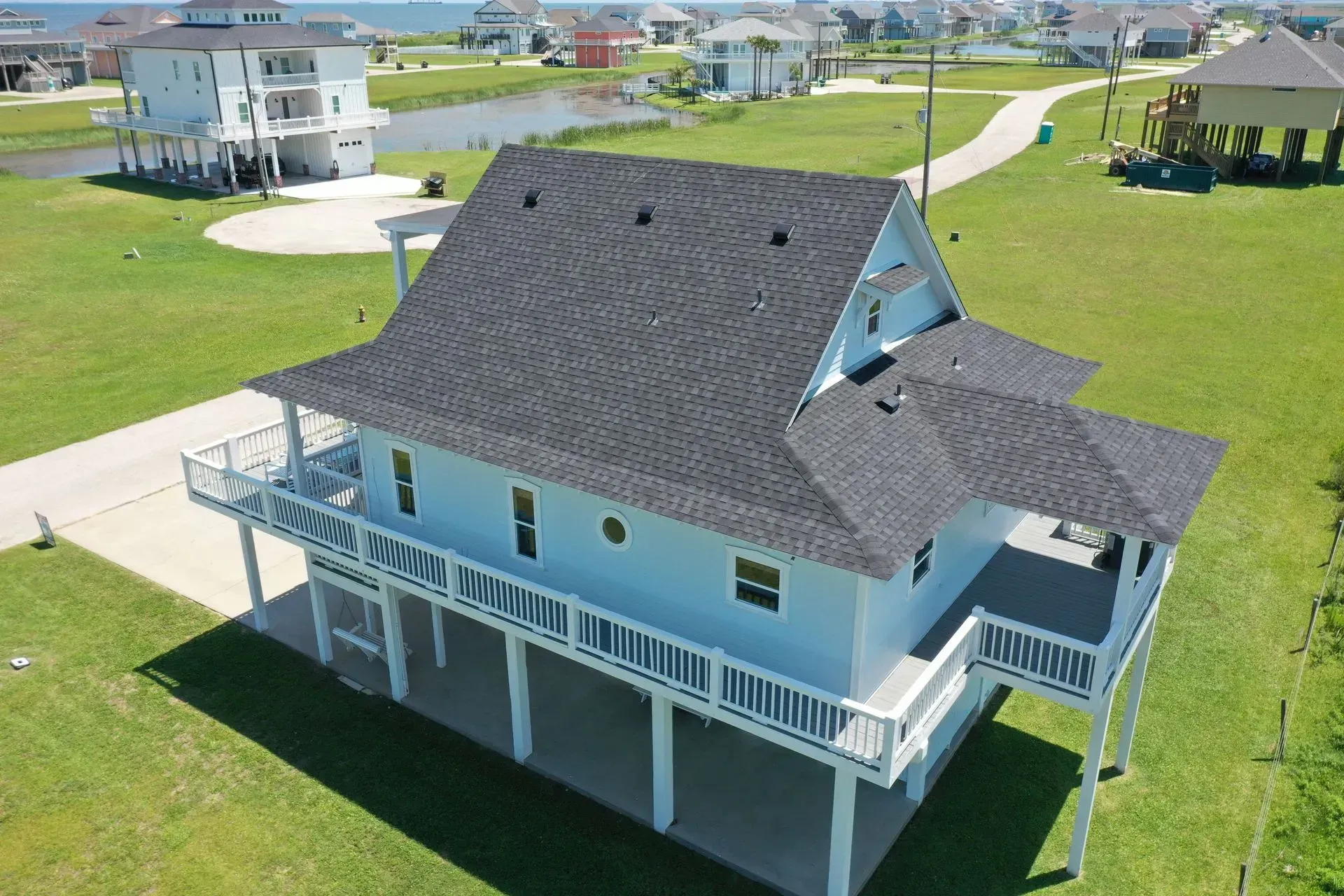 Blue beach house on stilts with a dark gray roof, surrounded by green grass.