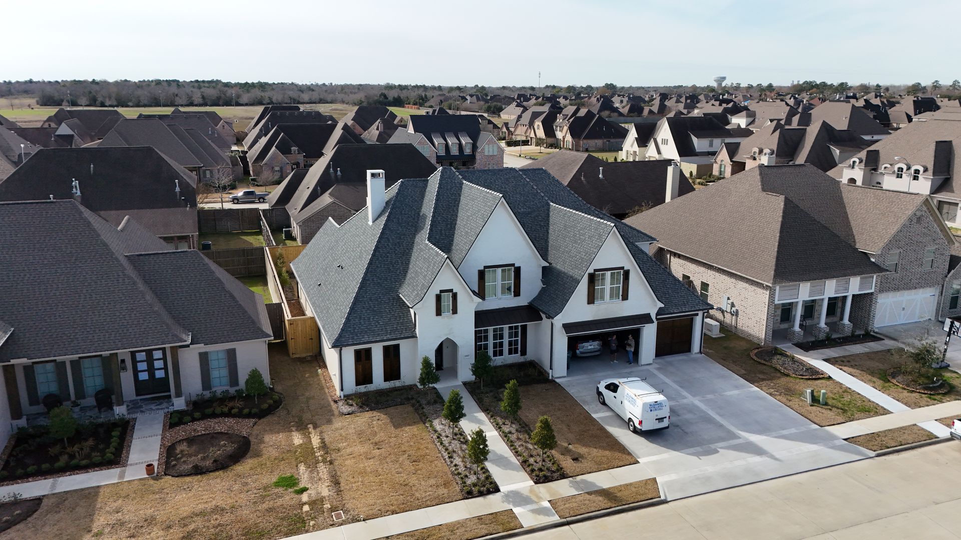 Aerial view of a white house with a gray roof and a driveway in a suburban neighborhood.
