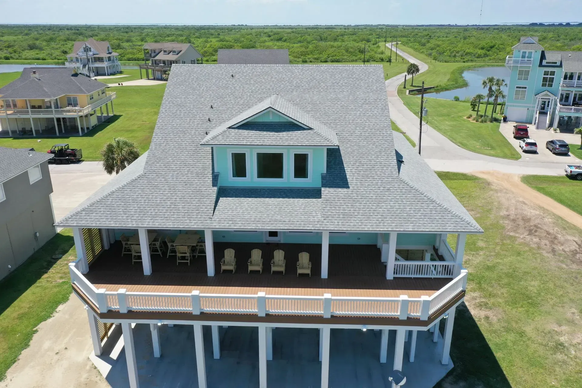 Beach house with a blue facade, large deck, and gray roof, in a grassy area.