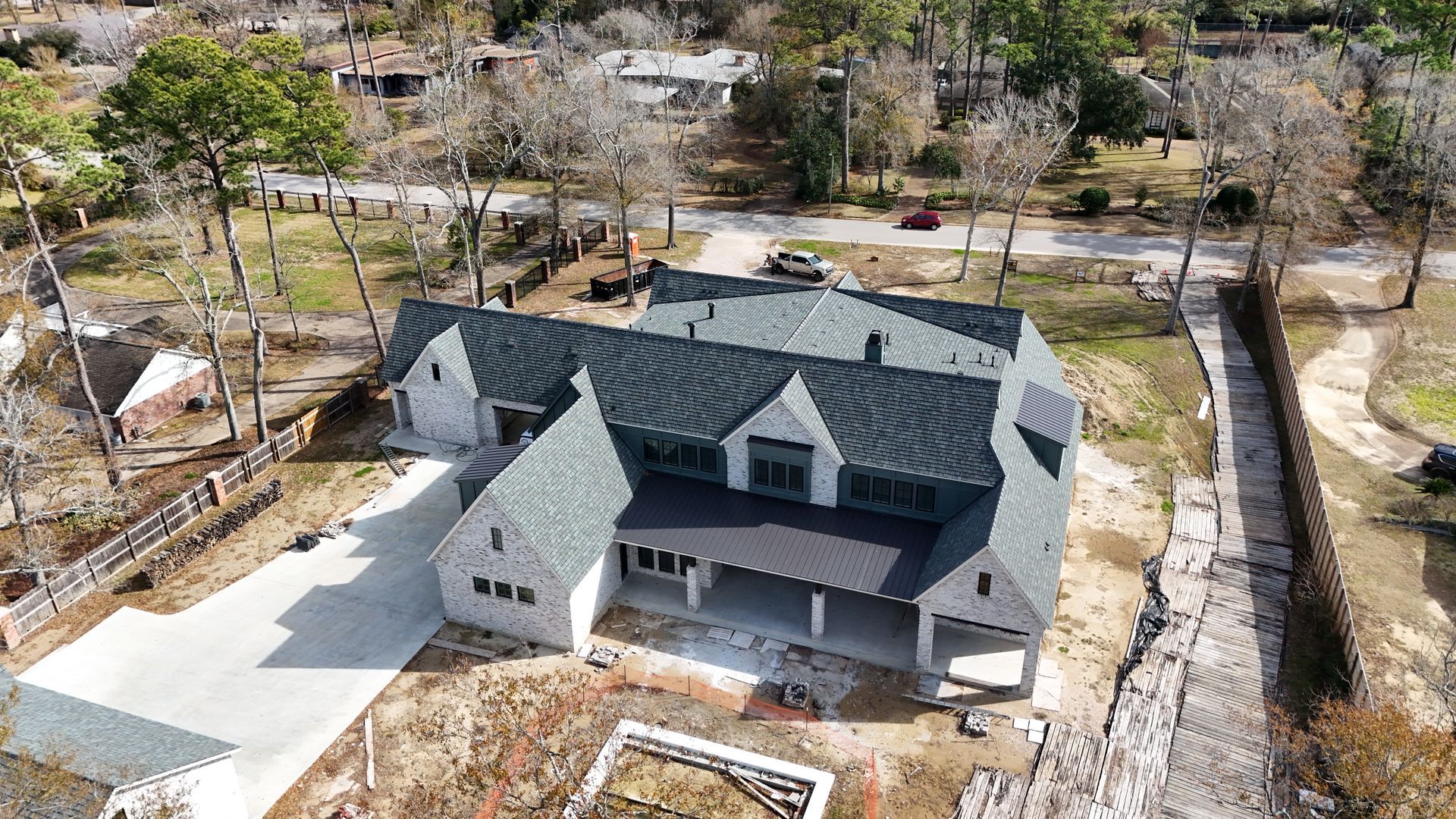 Aerial view of a white and gray house with a long driveway under construction, surrounded by trees.