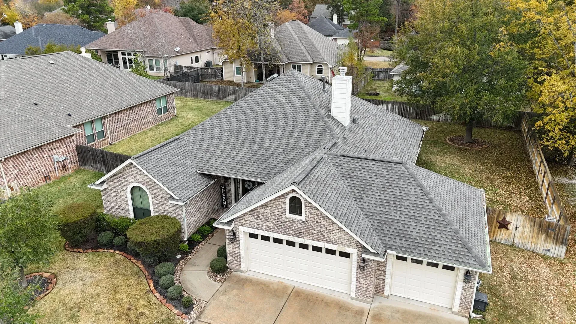 Aerial view of a suburban house with a gray roof and two-car garage. Overcast day.